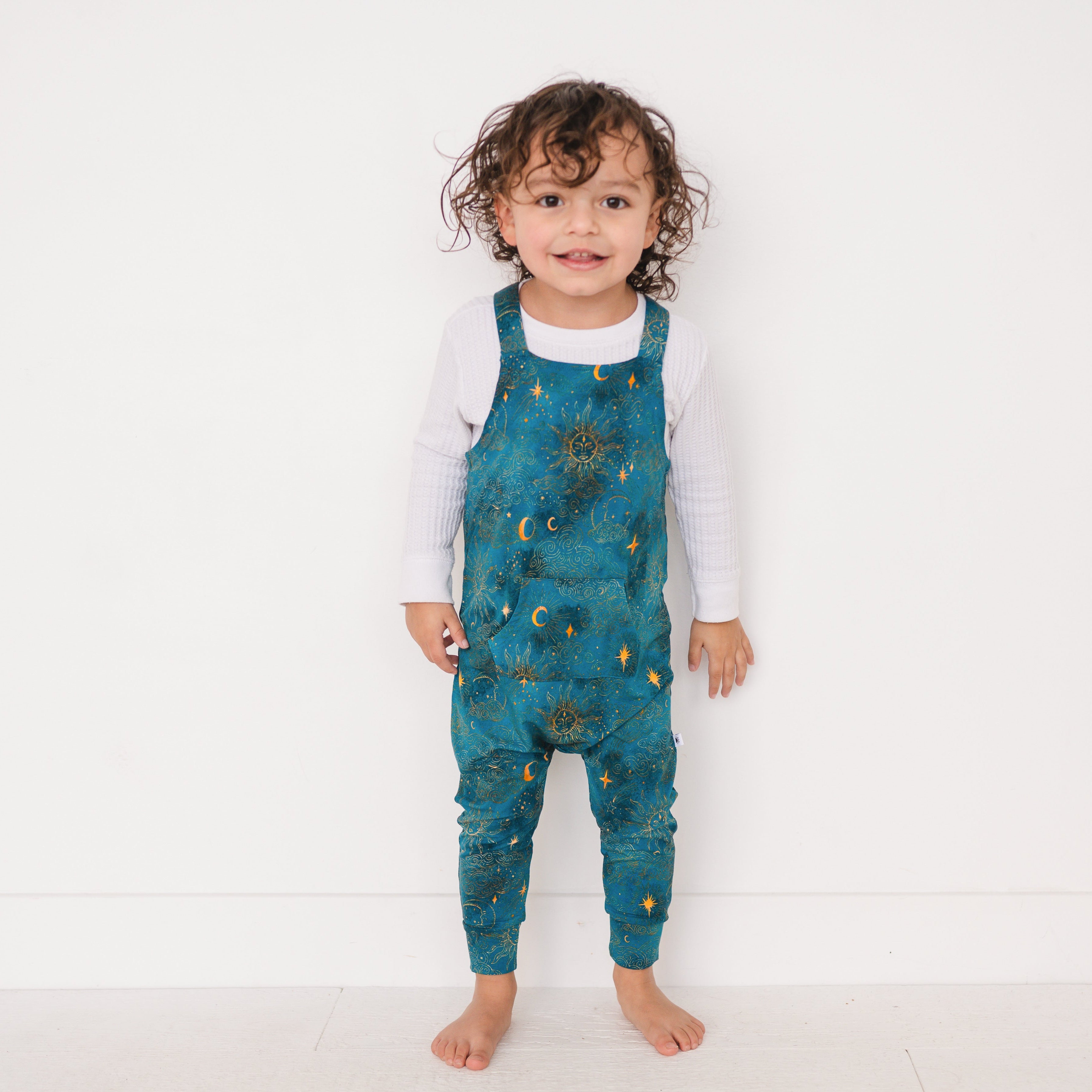 Toddler wearing teal overalls with a celestial sun and moon print.