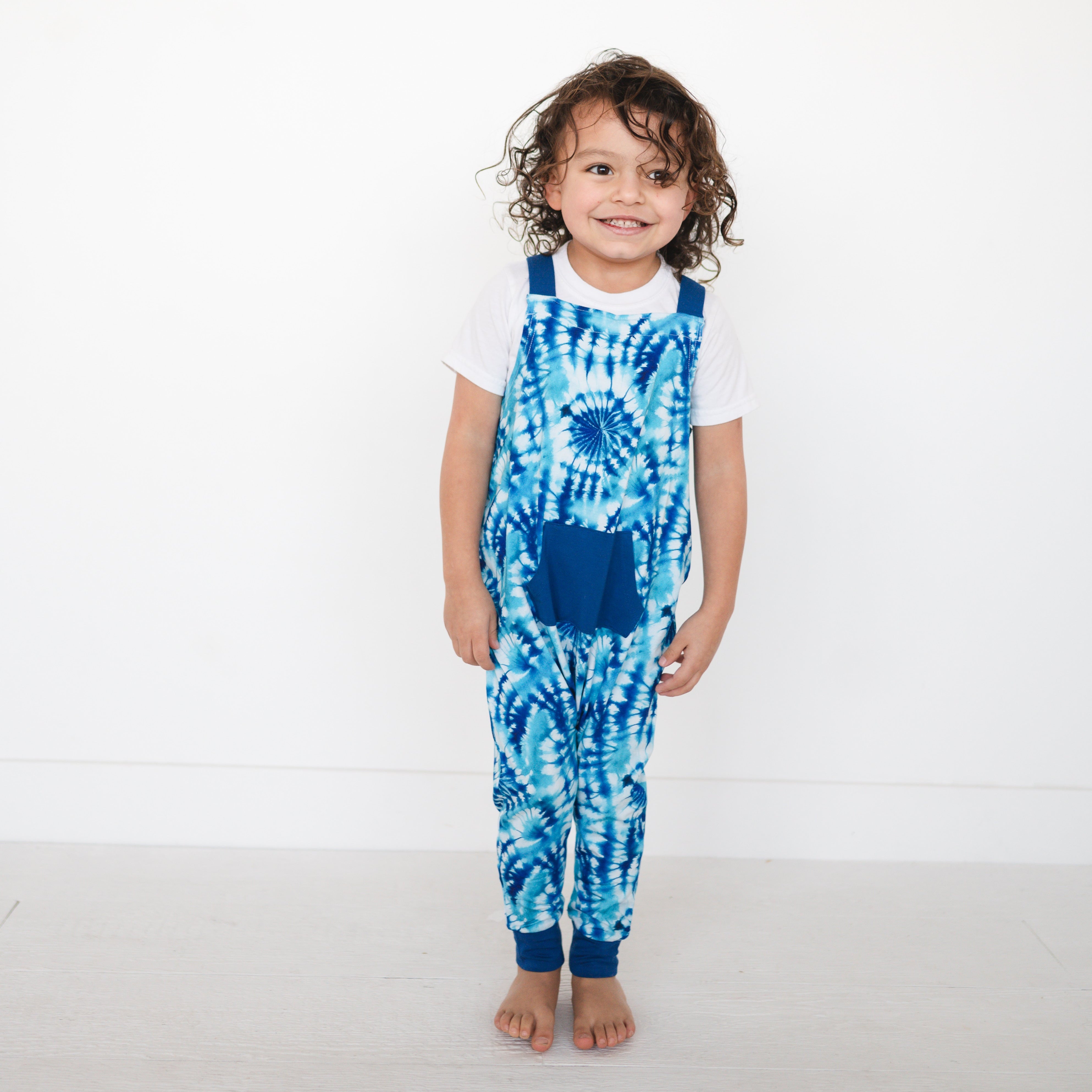 A child wears blue tie-dye overalls over a white t-shirt.