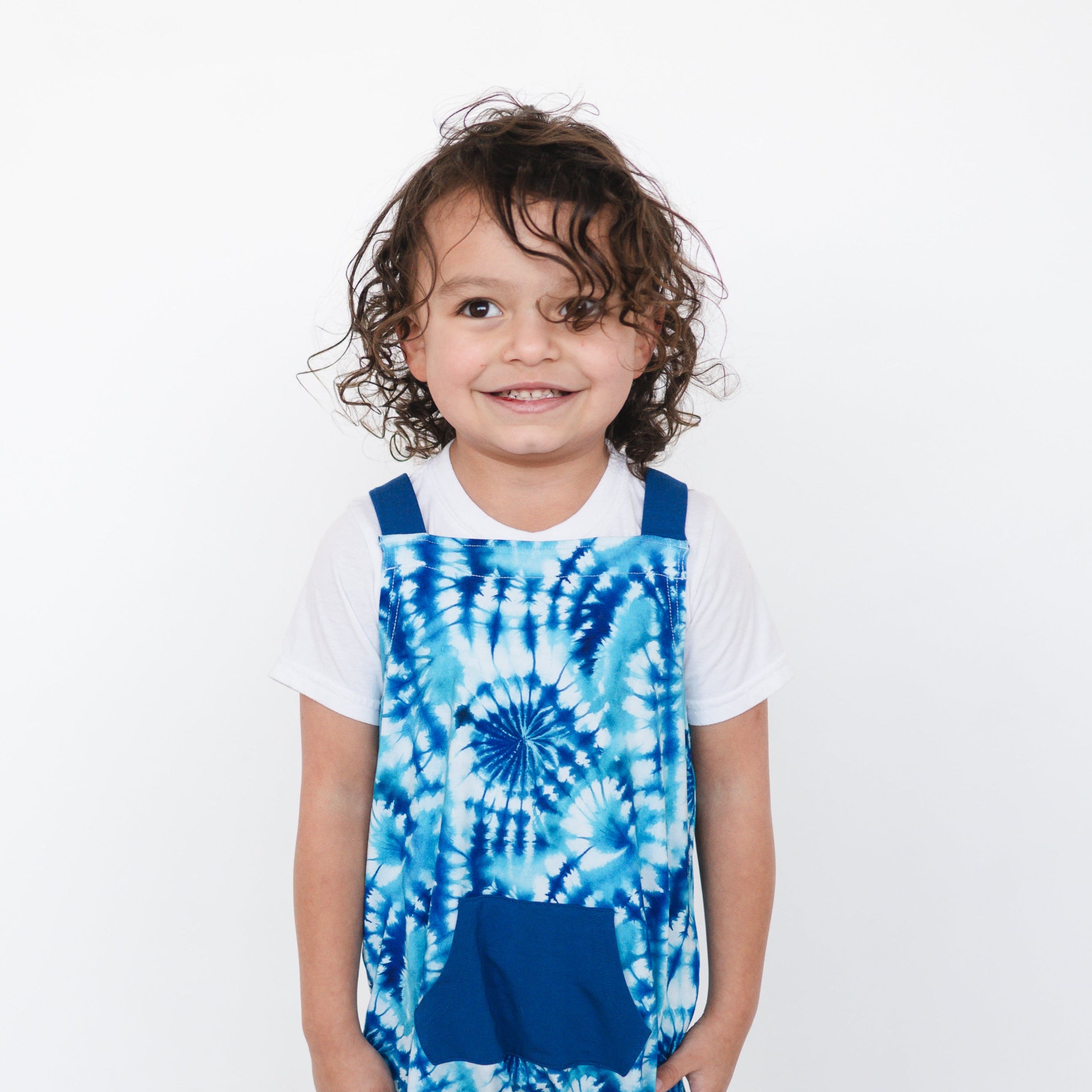 A young child wears blue tie-dye overalls over a white t-shirt.