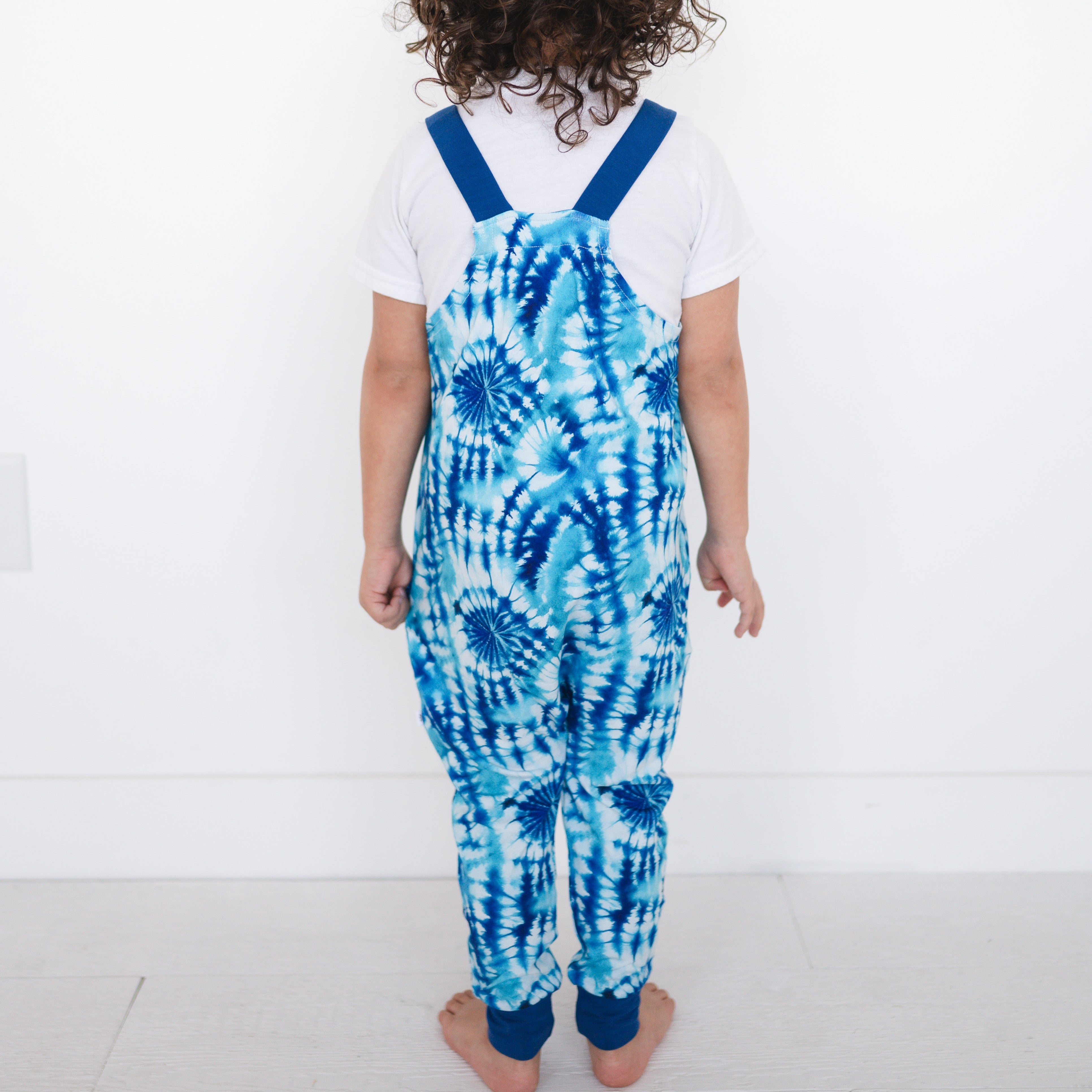 Toddler overalls with a blue tie-dye print and blue straps.
