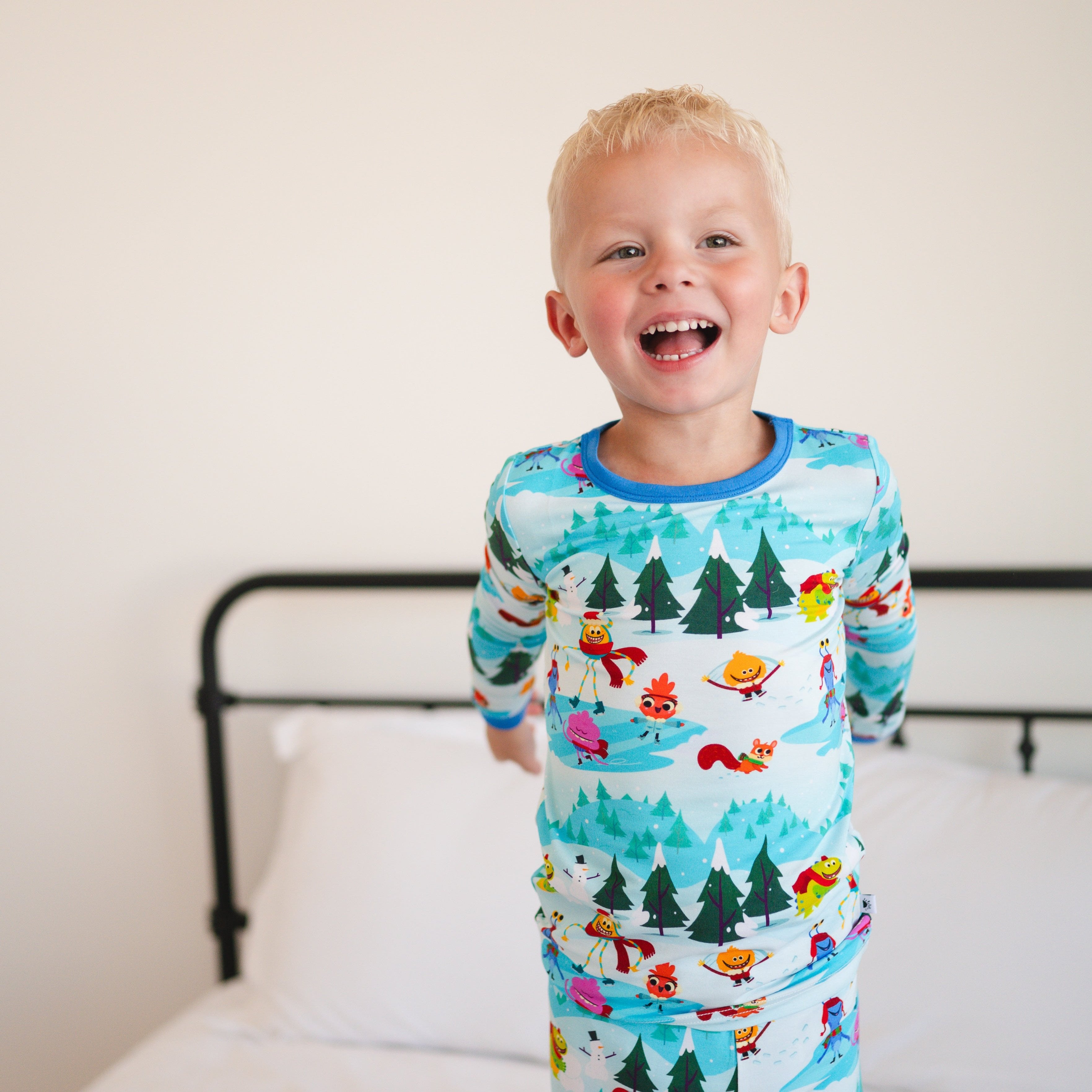 A young boy smiles widely wearing light blue pajamas with a winter scene print.