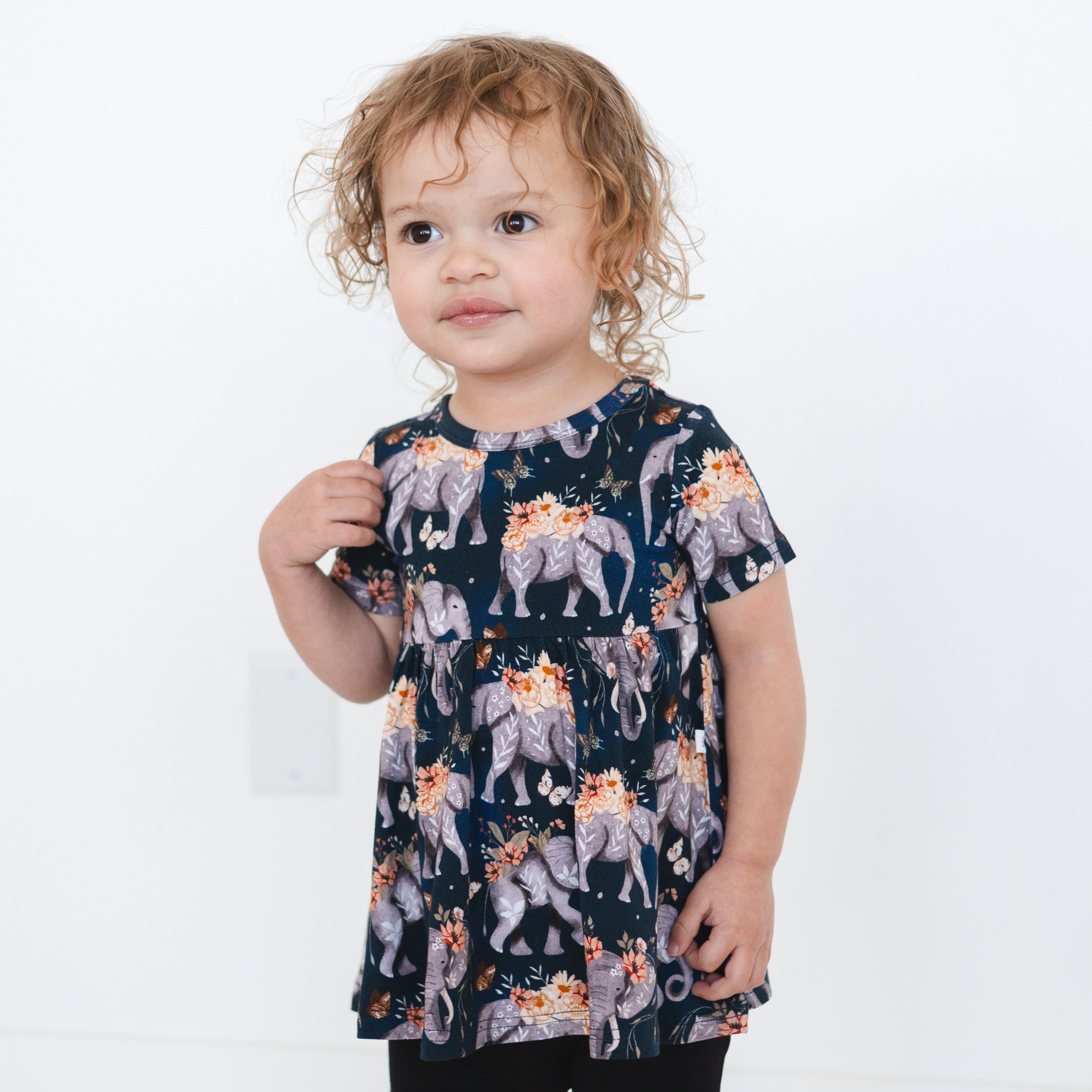 A young girl wears a navy peplum top with an elephant and floral print.
