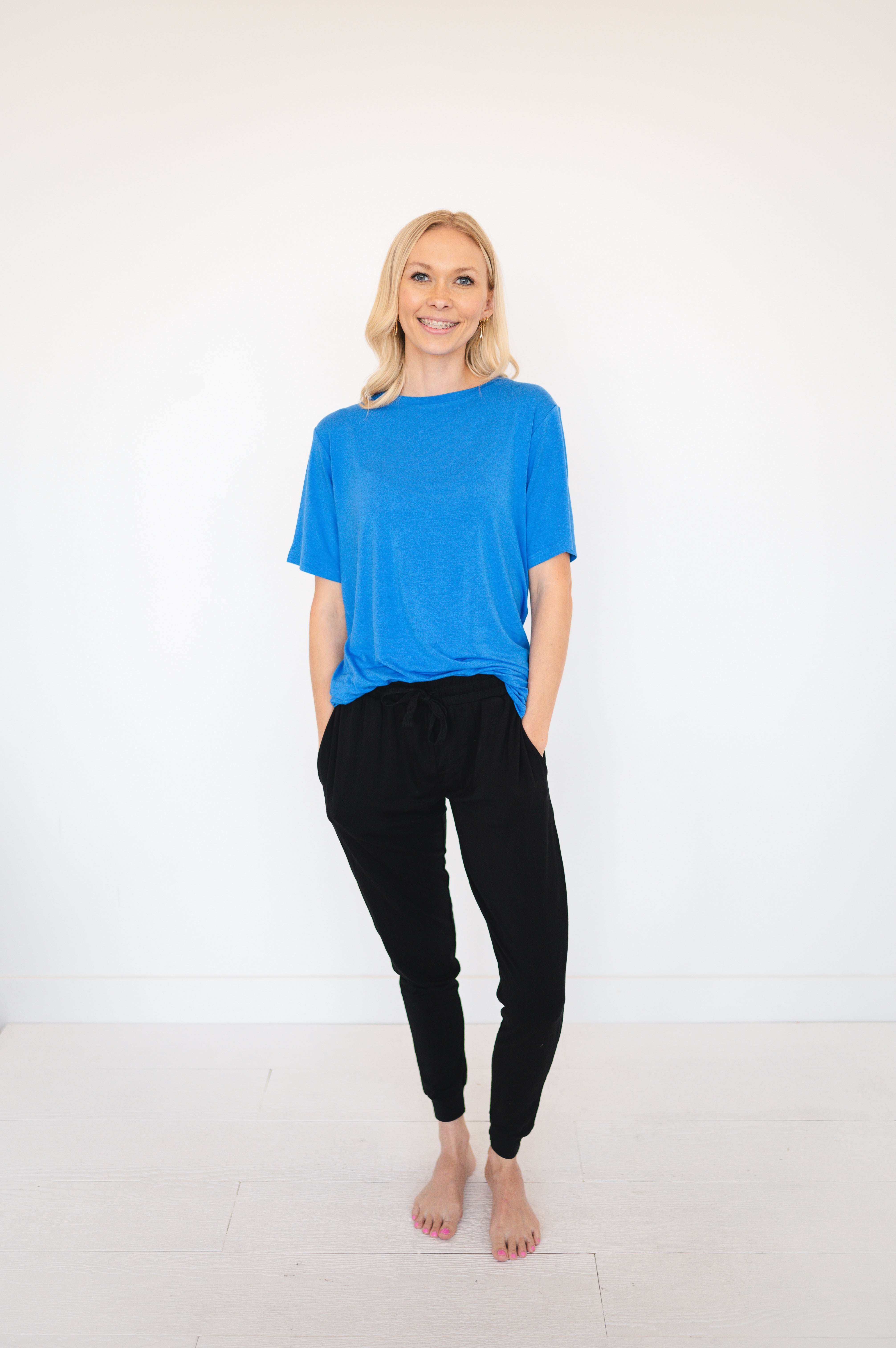 A woman stands wearing a blue t-shirt and black joggers.