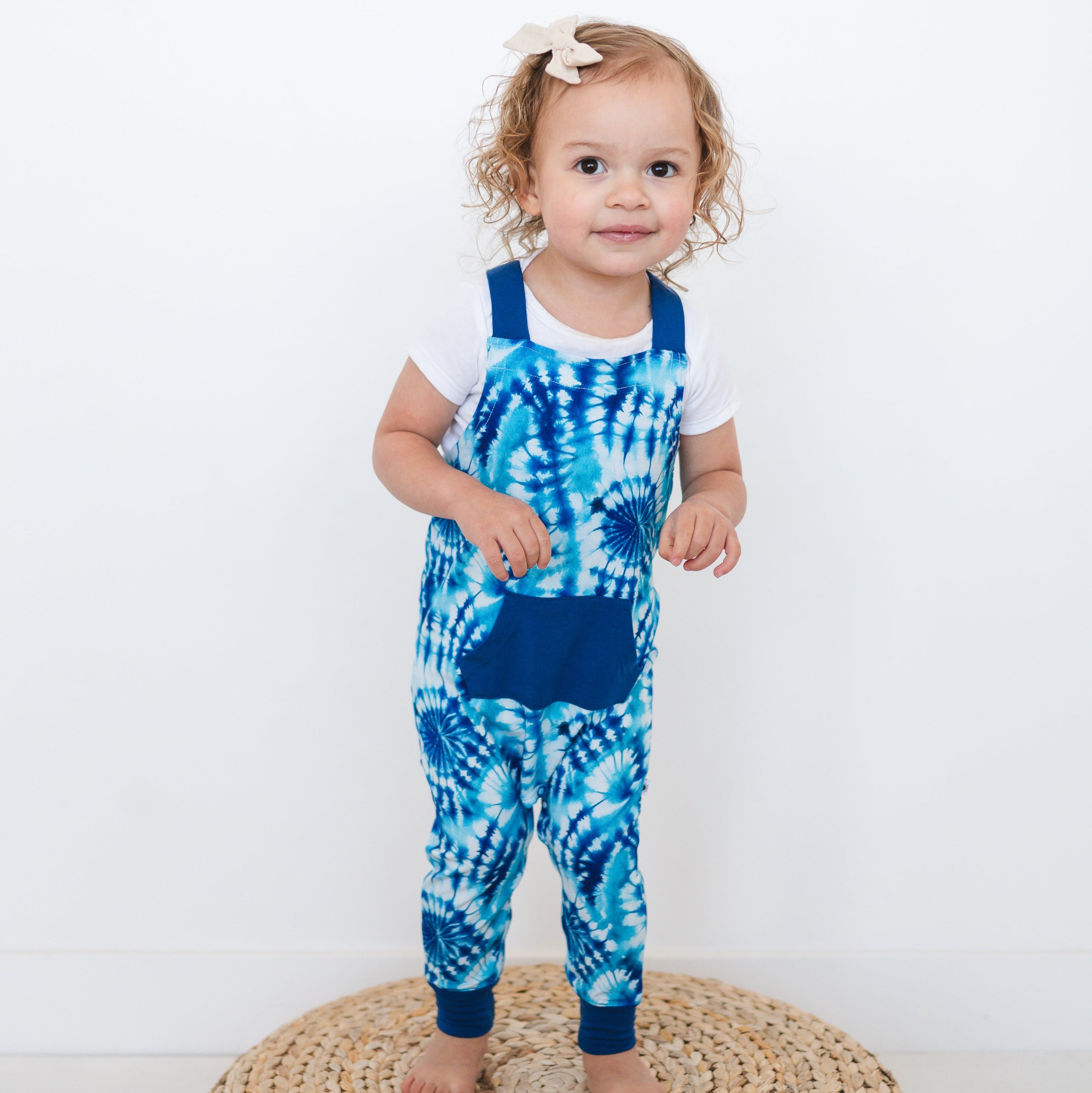 Toddler girl in blue tie-dye bamboo overalls and white t-shirt.