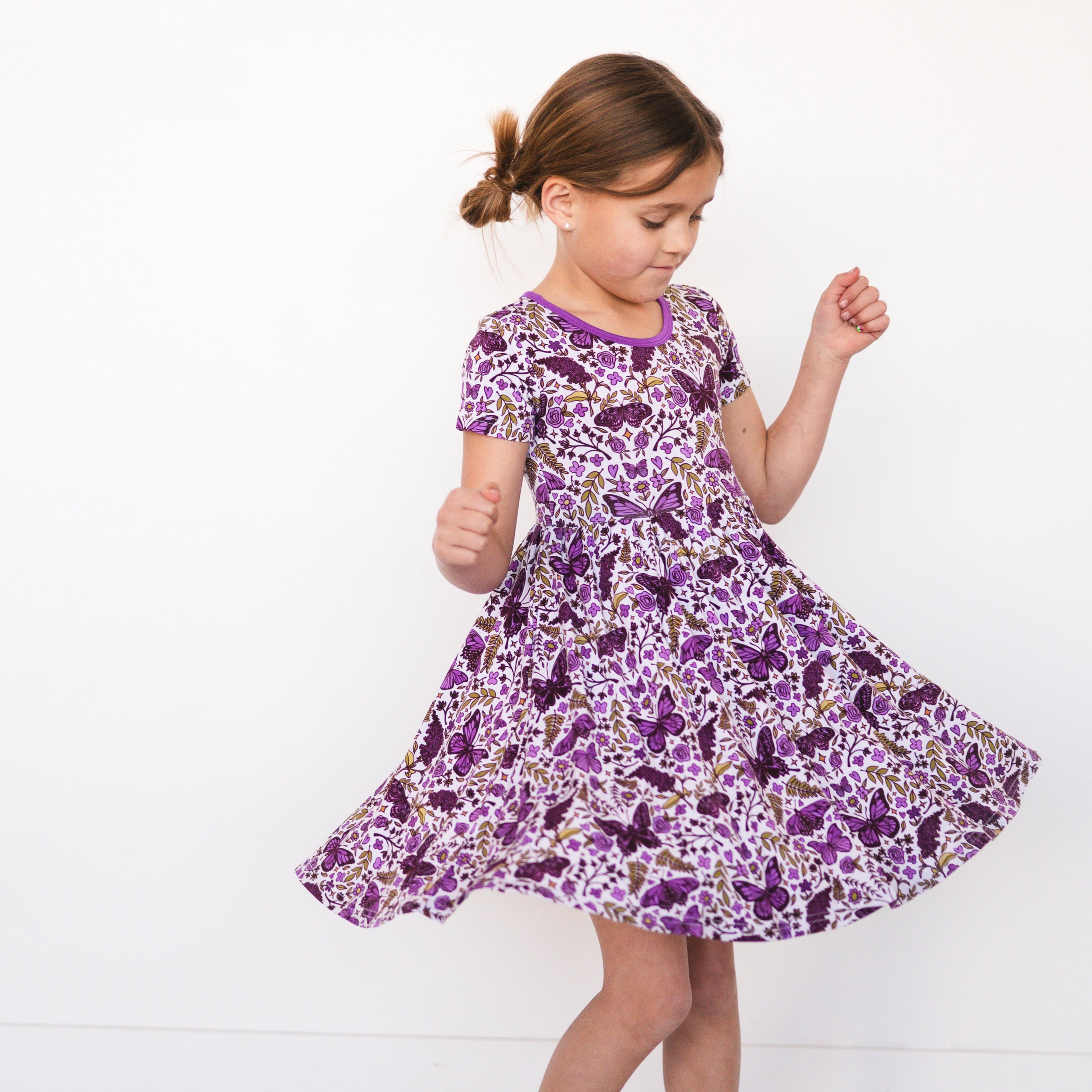Girl in a purple butterfly garden print dress twirling.