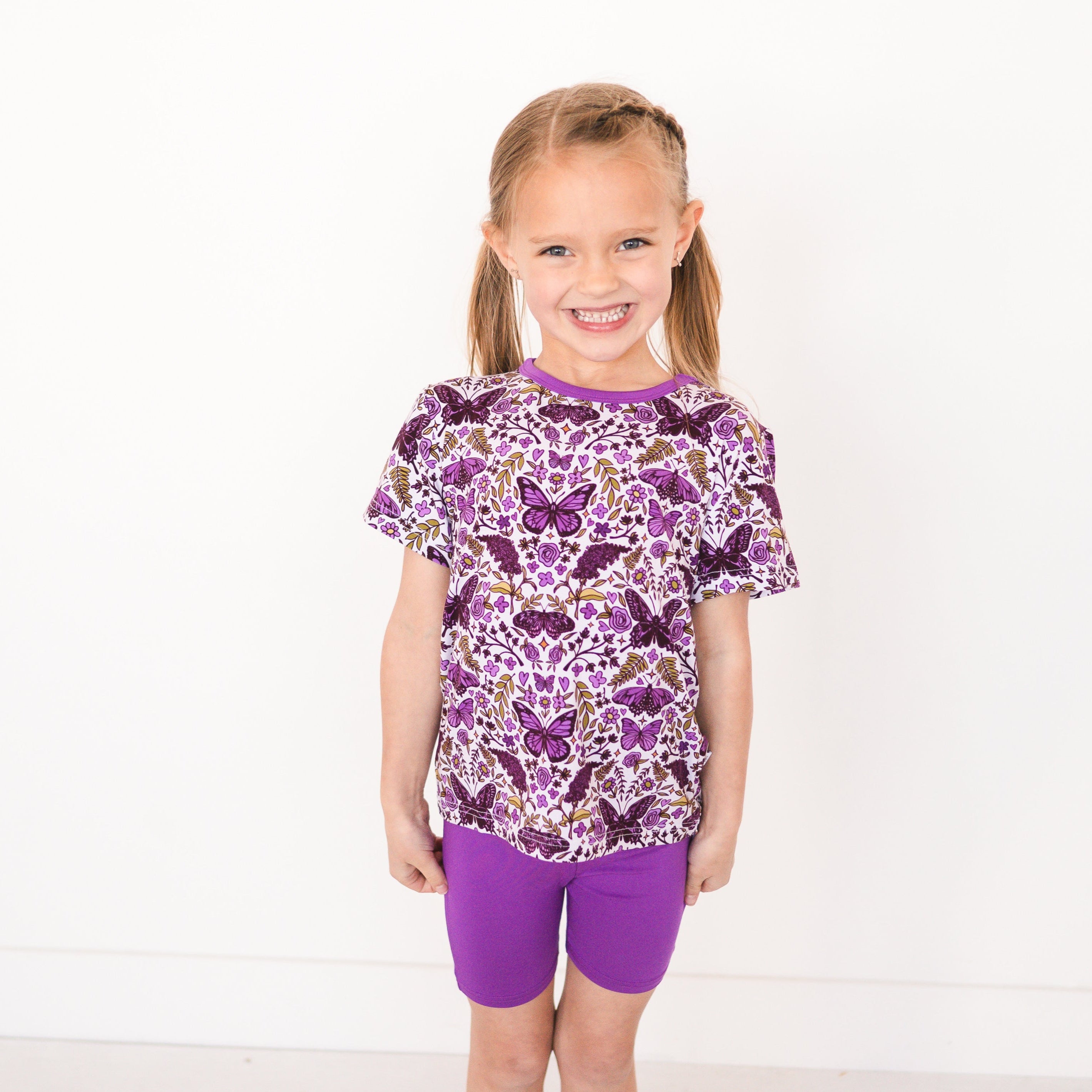 Girl wearing a purple butterfly print t-shirt and purple biker shorts.