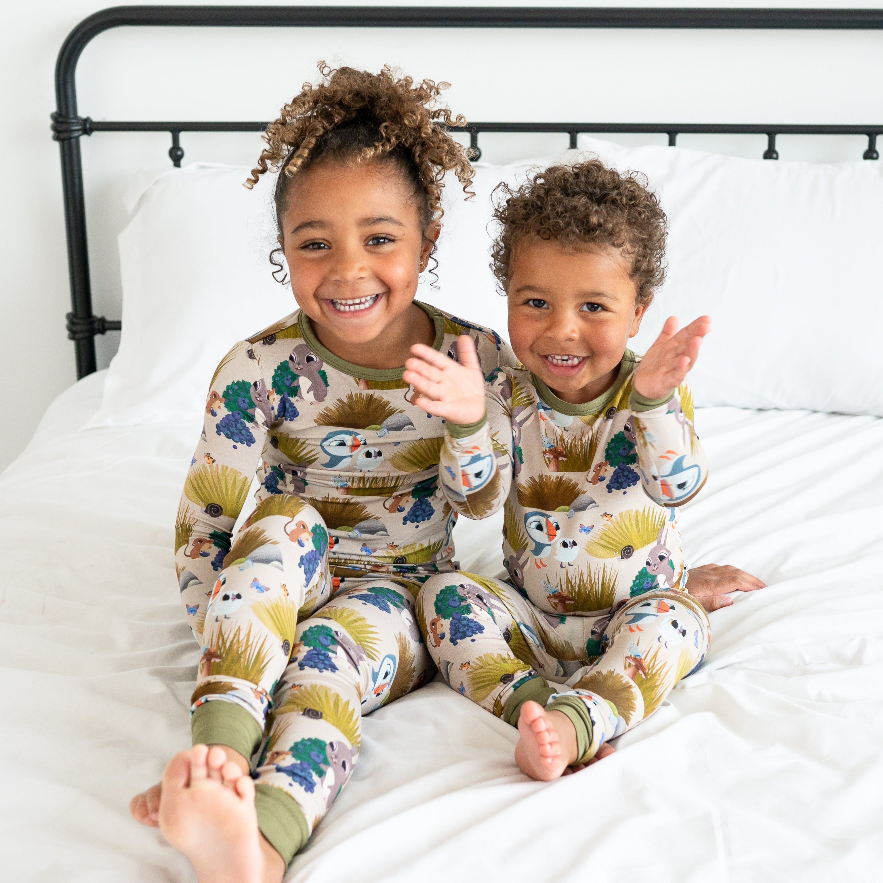 Two children in Puffin Rock™ bamboo pajamas sit on a bed.