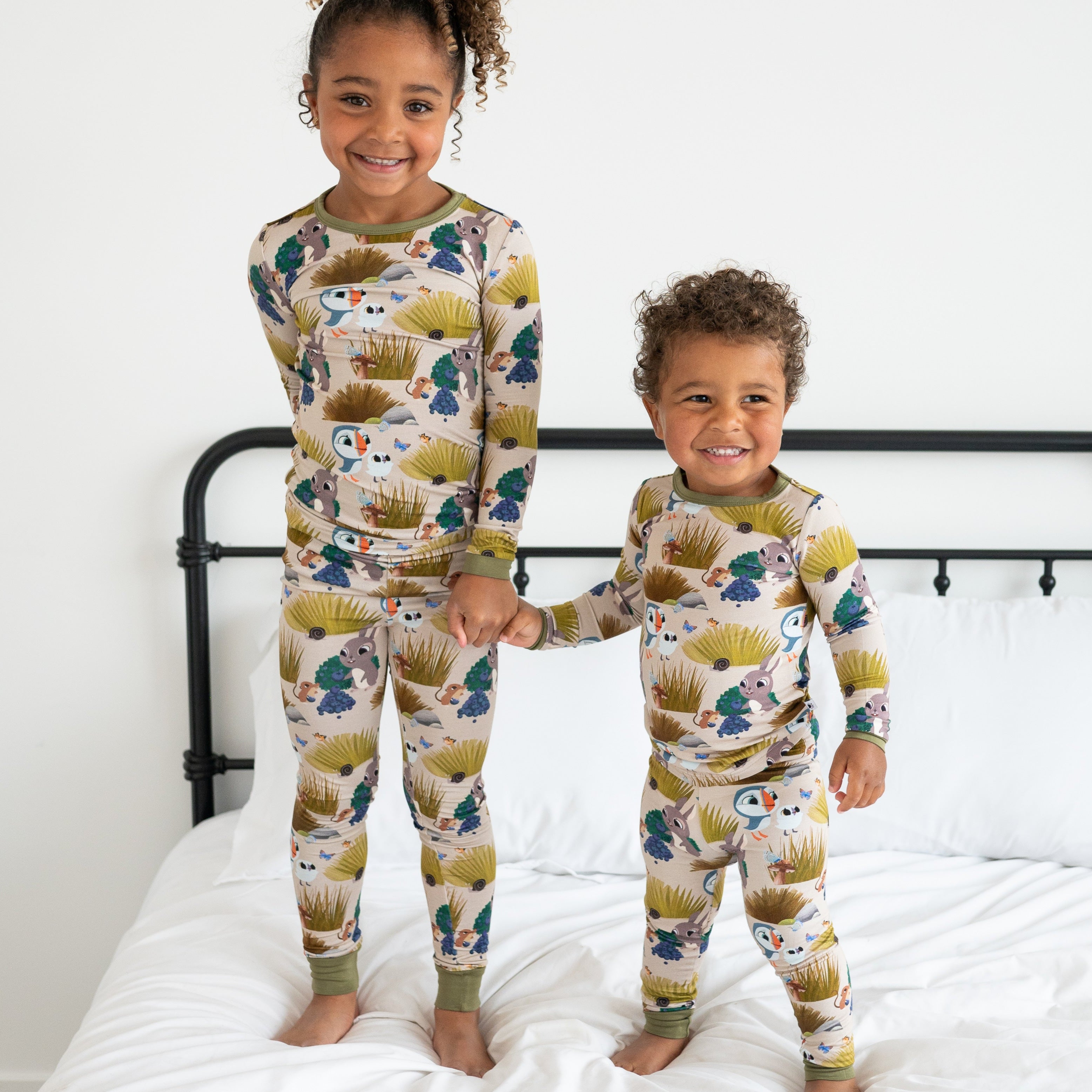 Two children in matching Puffin Rock bamboo pajamas with a woodland print.