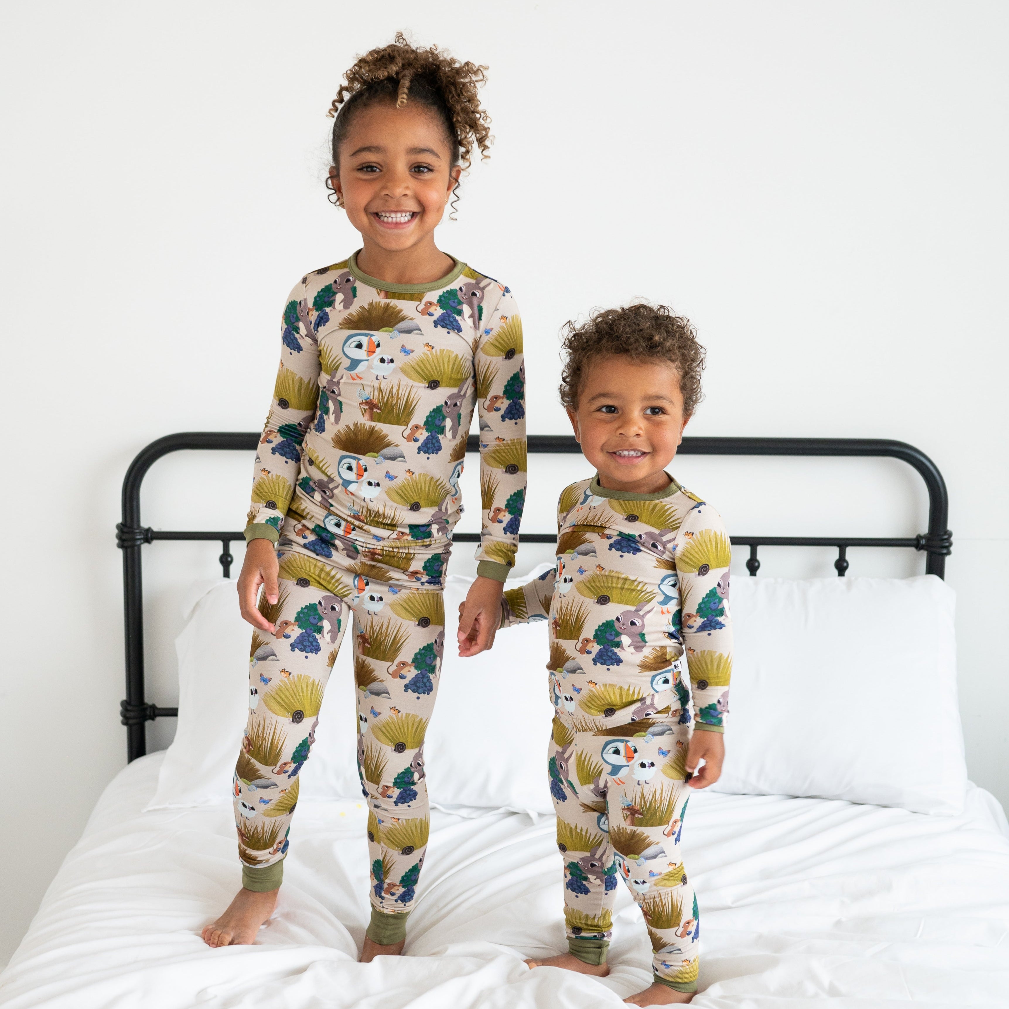 Two children in matching long-sleeved pajamas with a puffin and nature print.