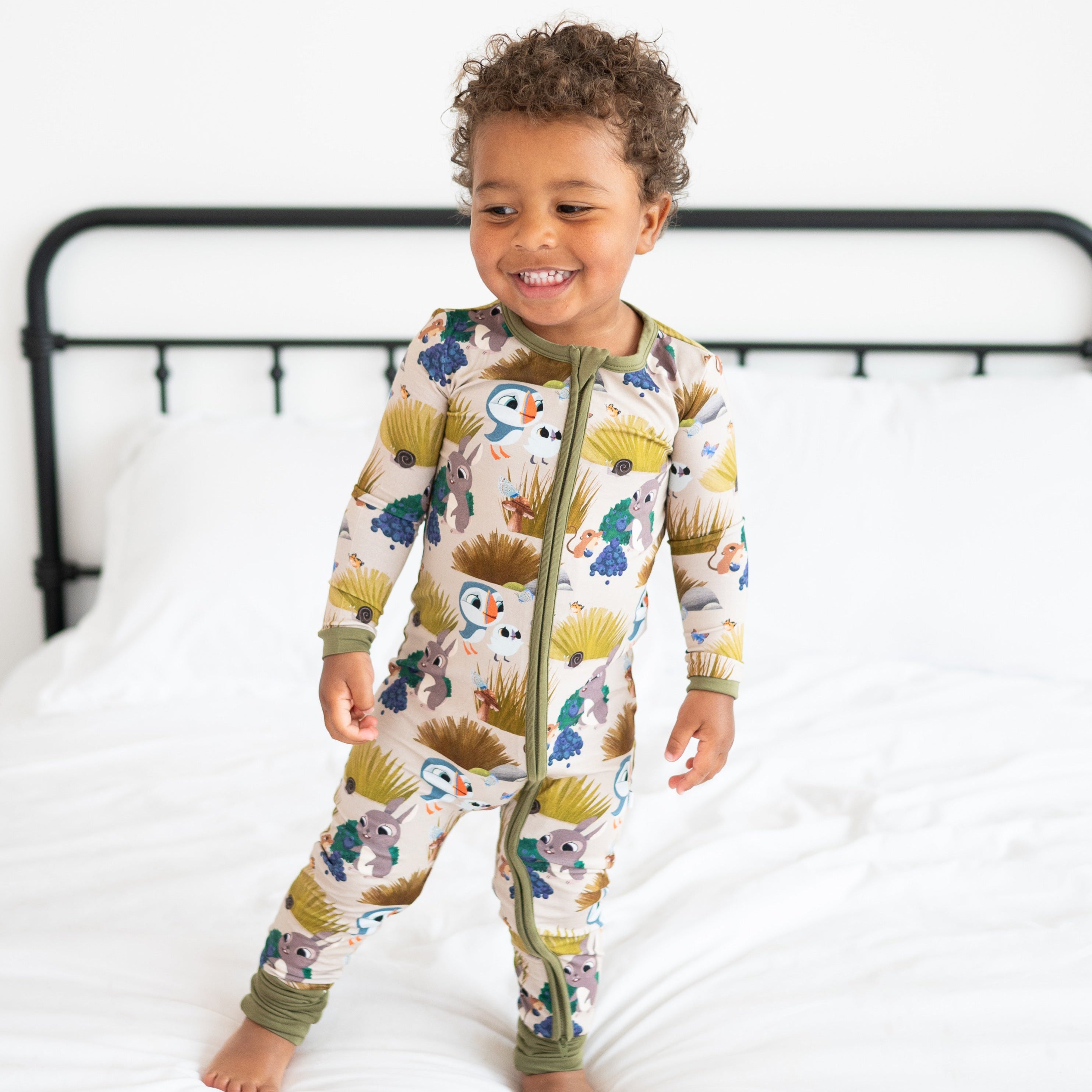 A toddler boy wears a tan zippered pajama set with a Puffin Rock print.