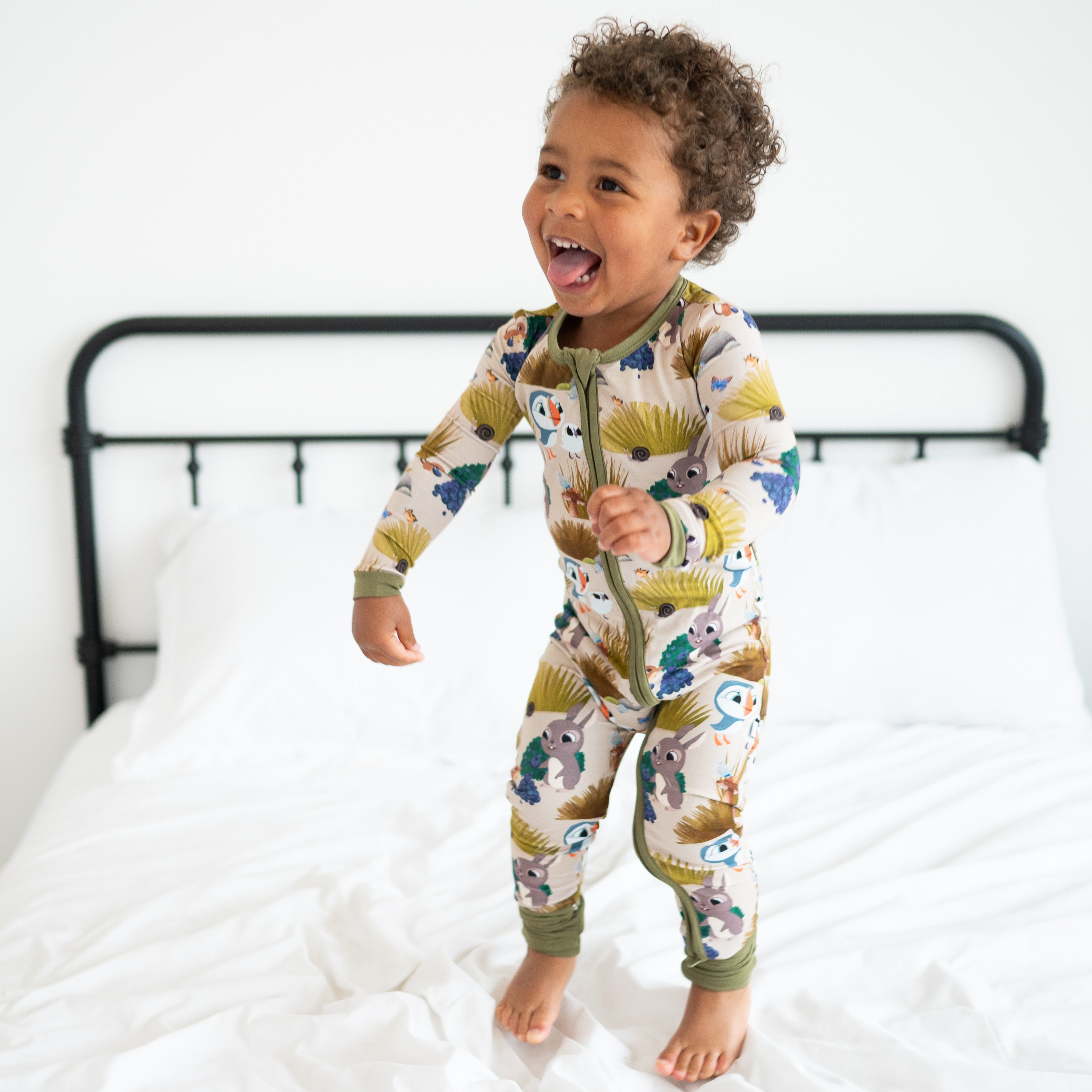 A happy toddler in a Puffin Rock themed bamboo pajama set jumps on a bed.