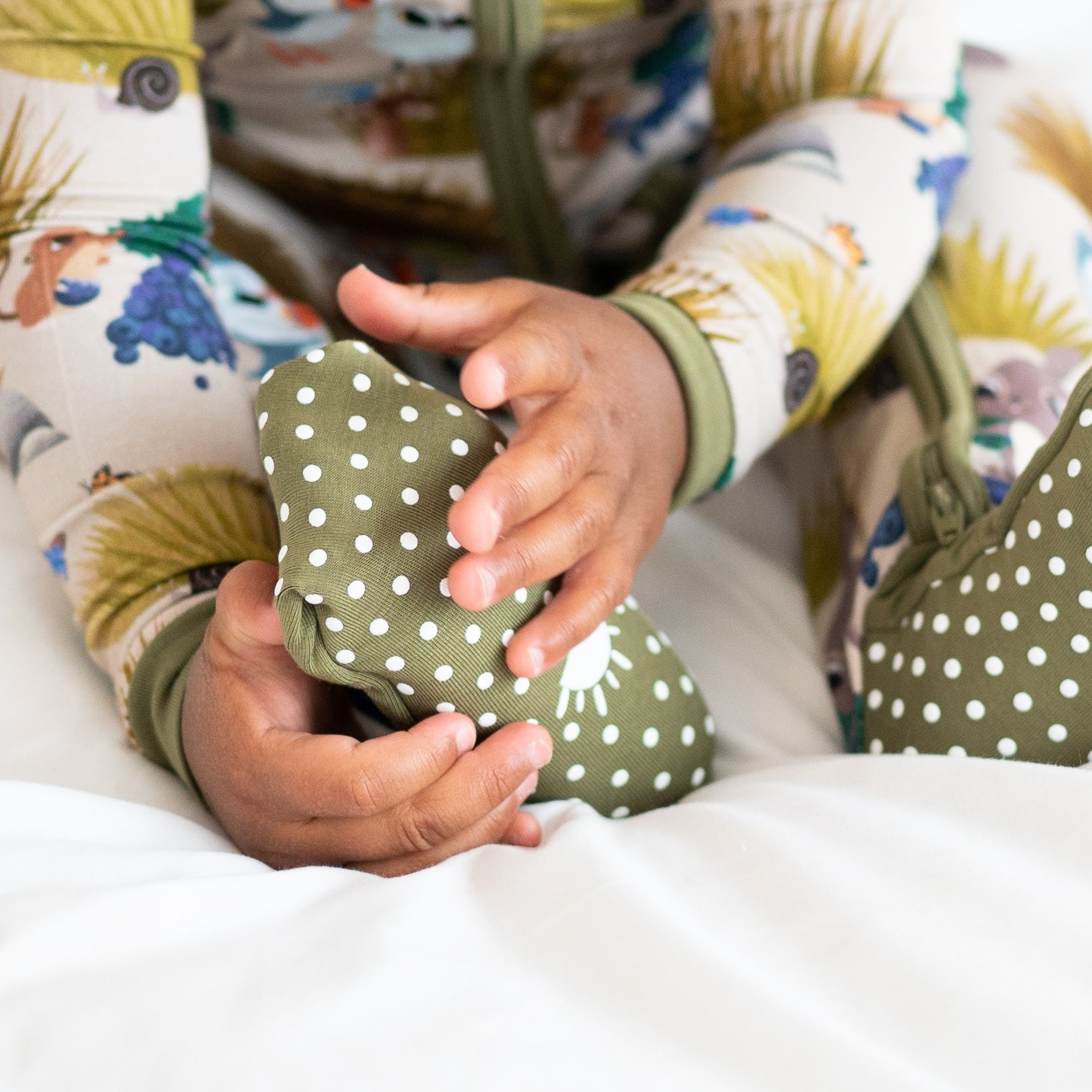 Baby's hands holding a green polka dot footed pajama.