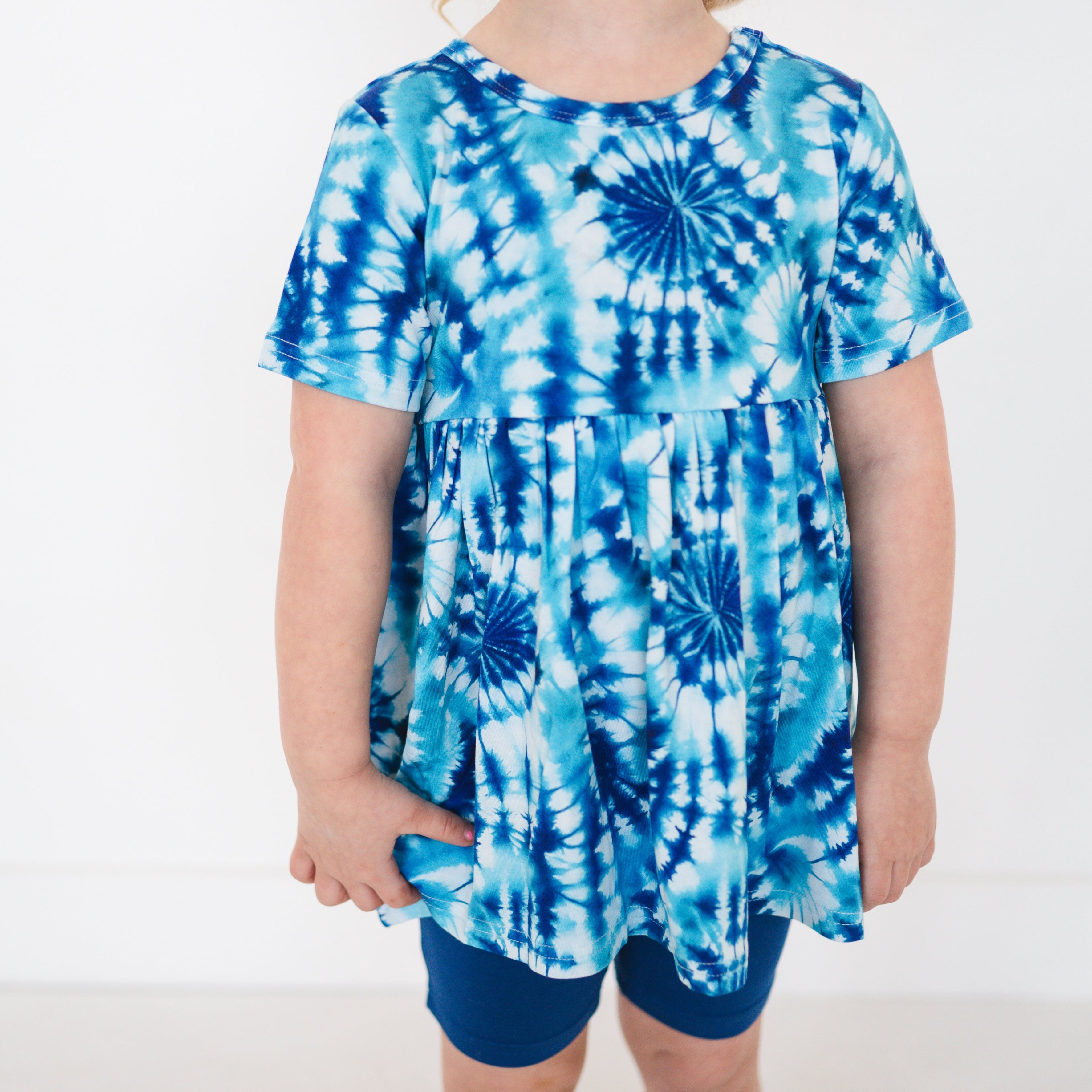 A girl wears a blue tie-dye peplum top and blue shorts.