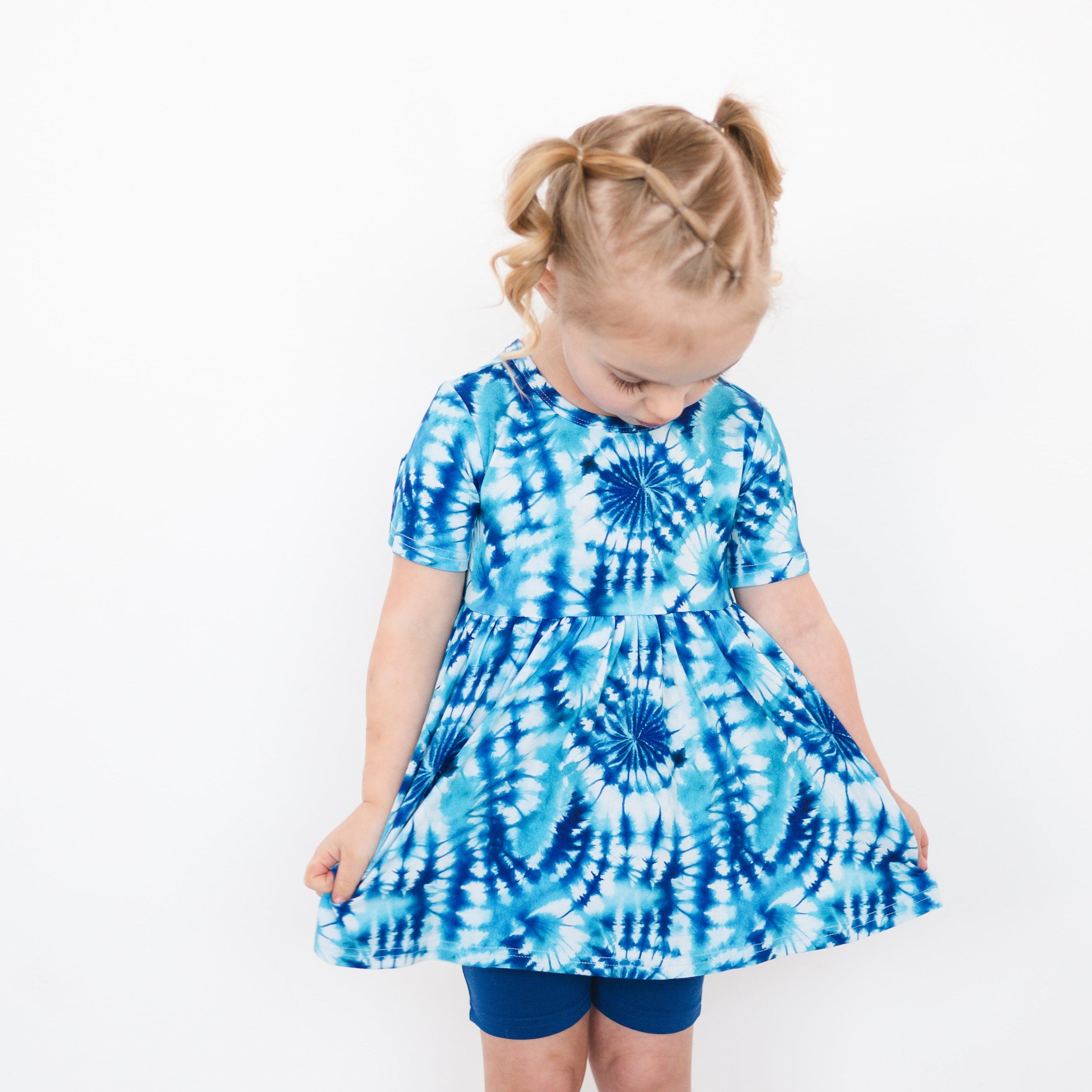 A young girl wears a blue and white tie-dye peplum top and blue shorts.