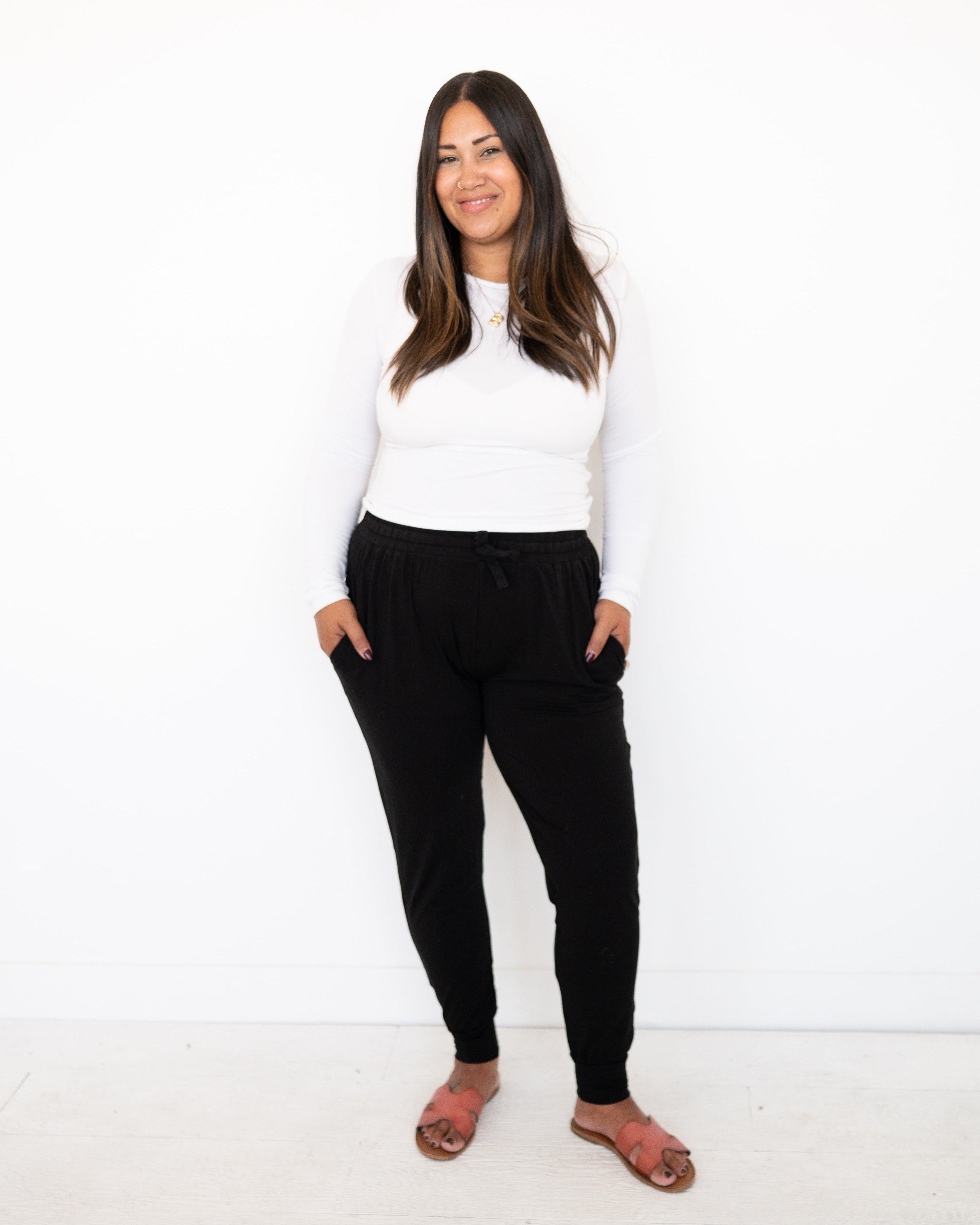 Woman wearing black Ploom Collective Luxe Bamboo joggers and a white long-sleeve shirt.