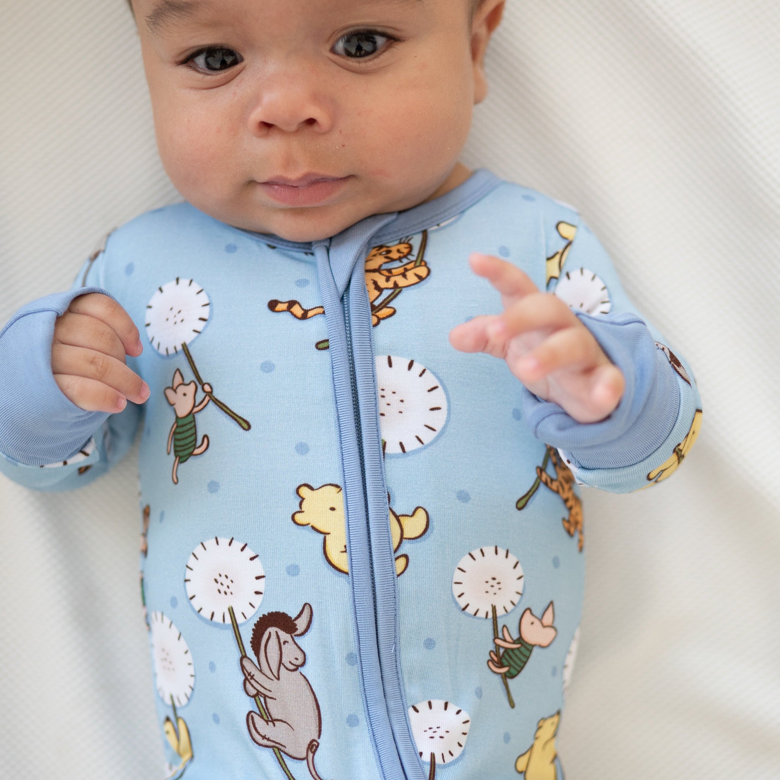 A baby wearing a light blue pajama set with Winnie the Pooh characters.