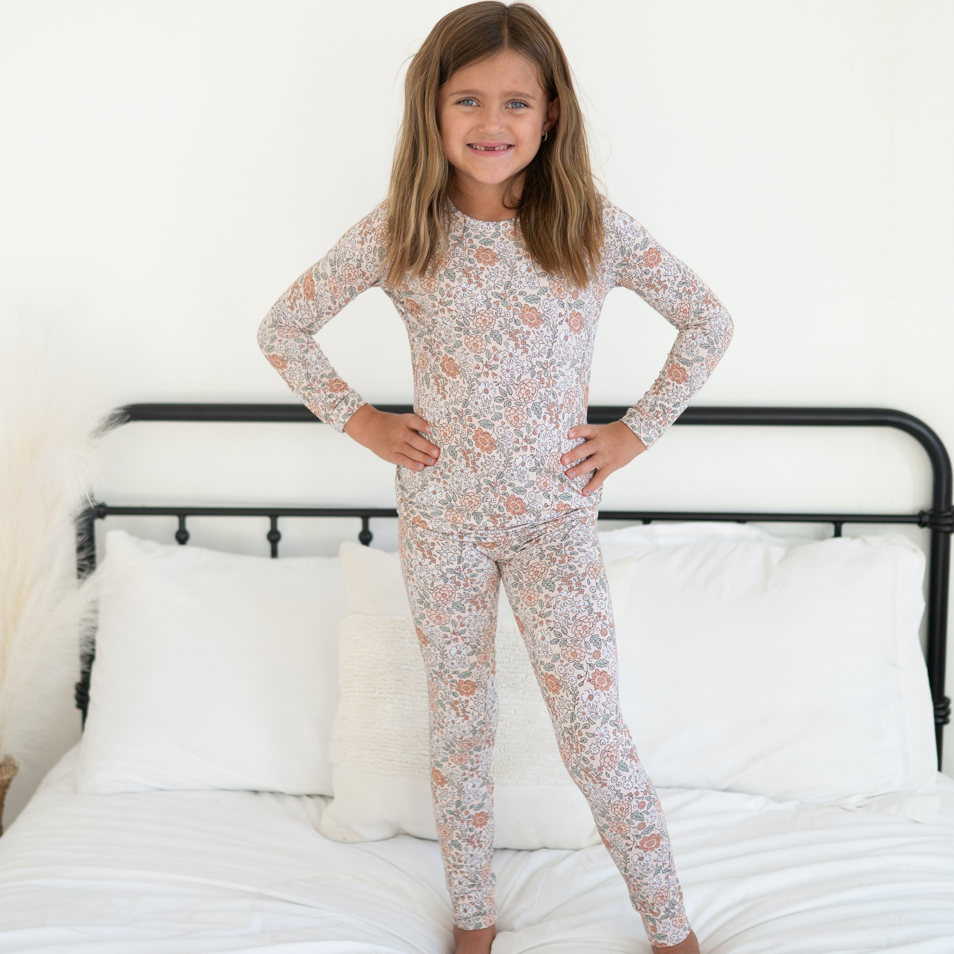 Young girl standing on bed in vintage floral long-sleeve pajama set.
