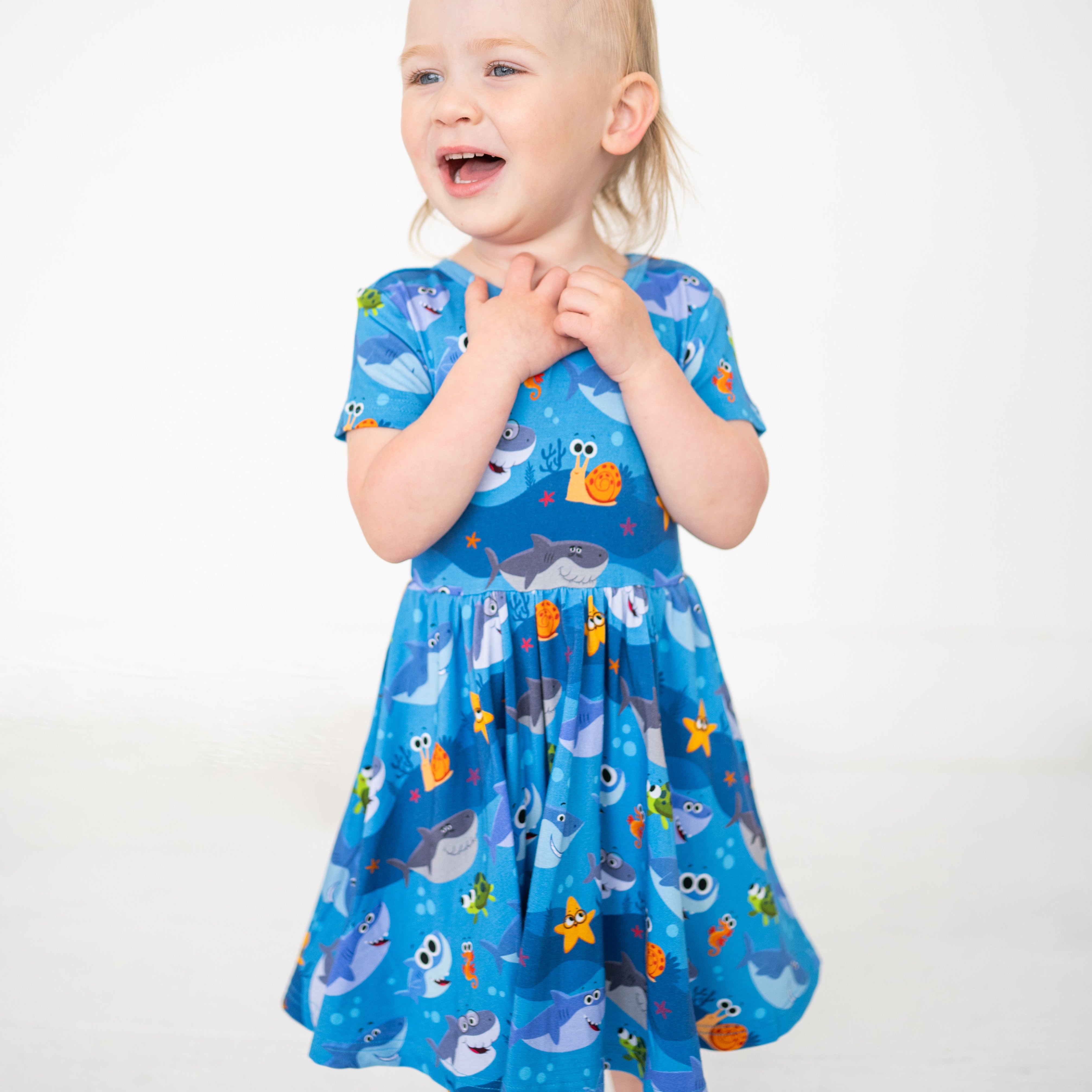 A young child wears a blue dress with a Baby Shark print.