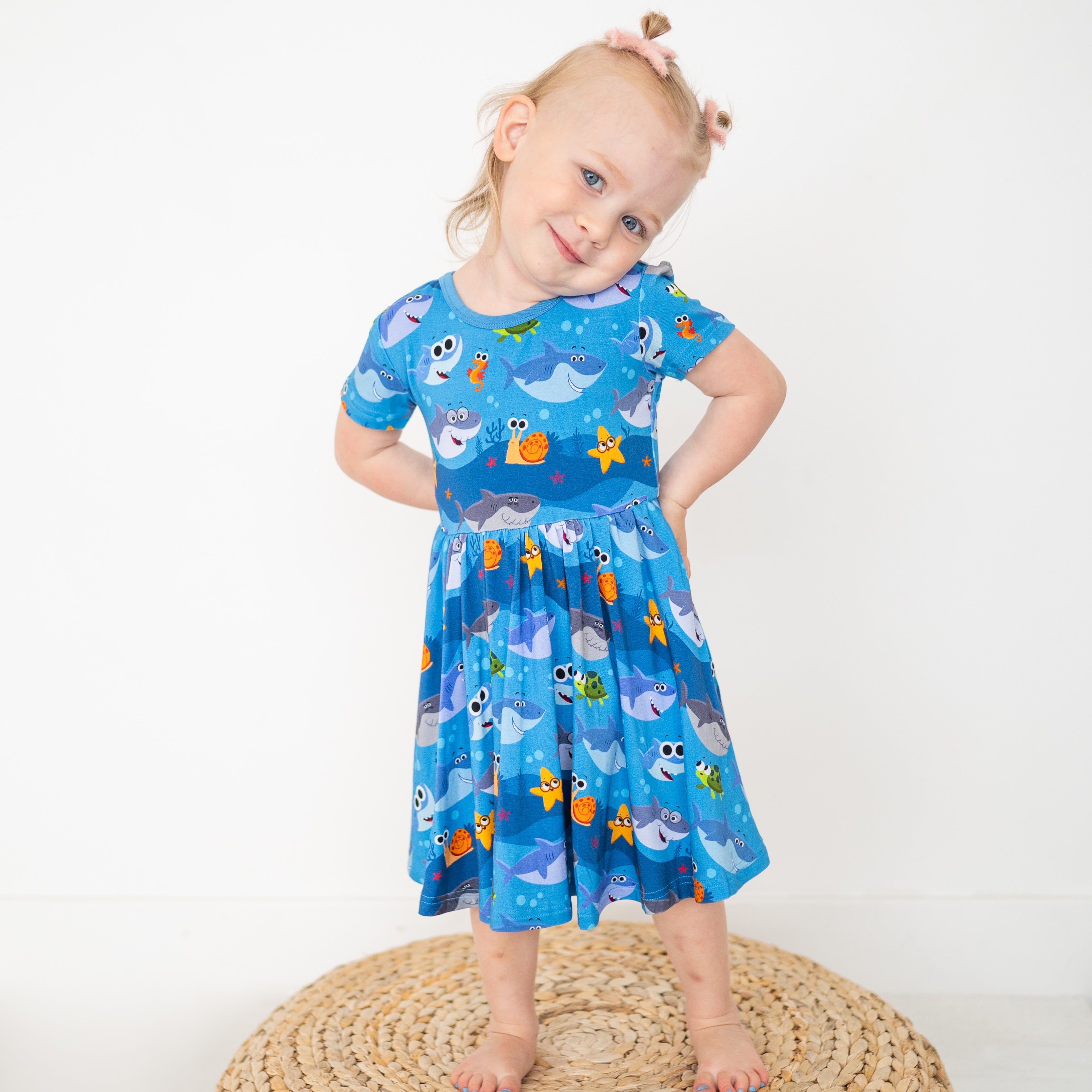 A young girl wears a blue dress with a Baby Shark print.