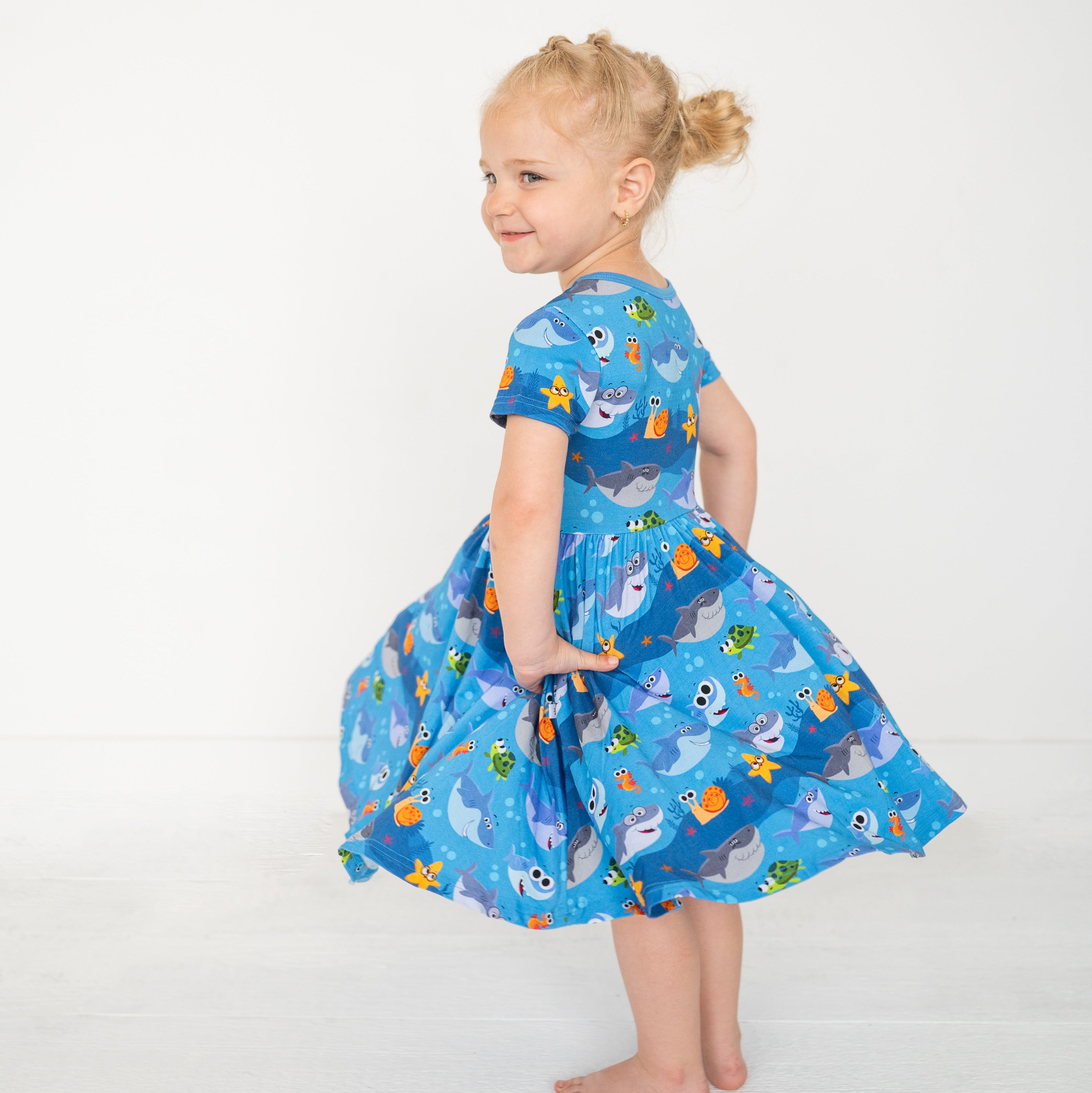 A young girl twirls in a blue dress with a Baby Shark print.