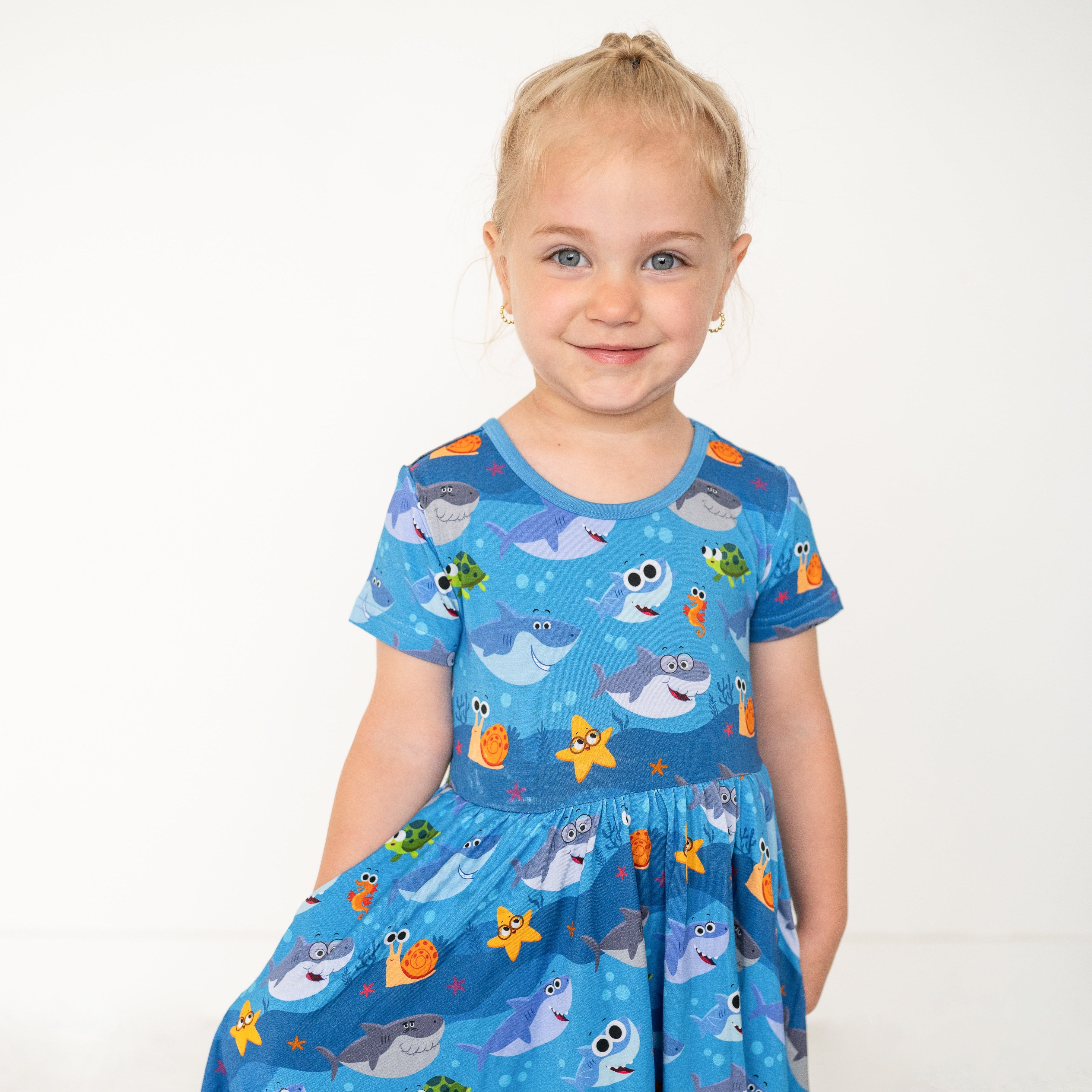 A young girl wears a blue dress with a Baby Shark print.