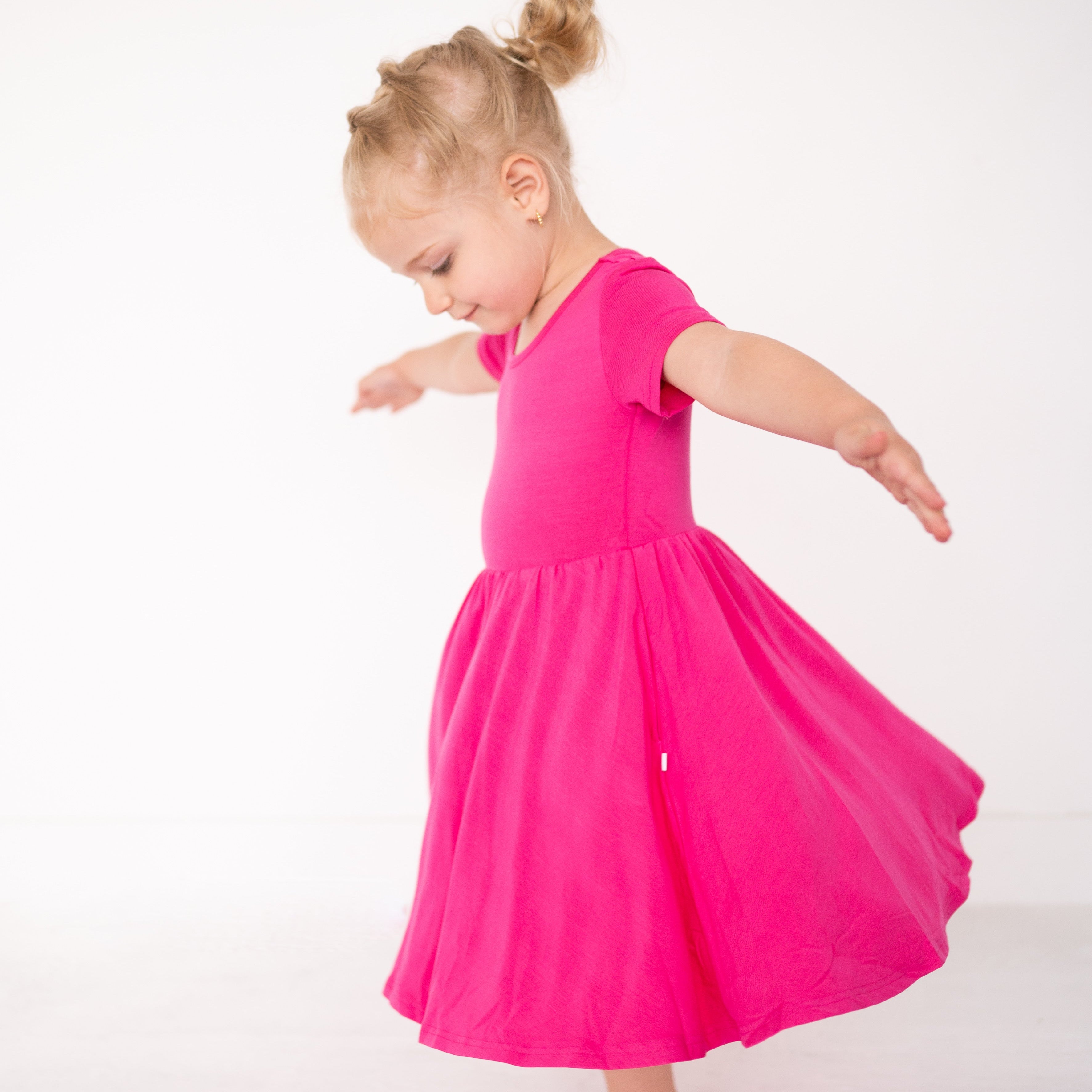 A young girl in a pink dress twirls against a white background.