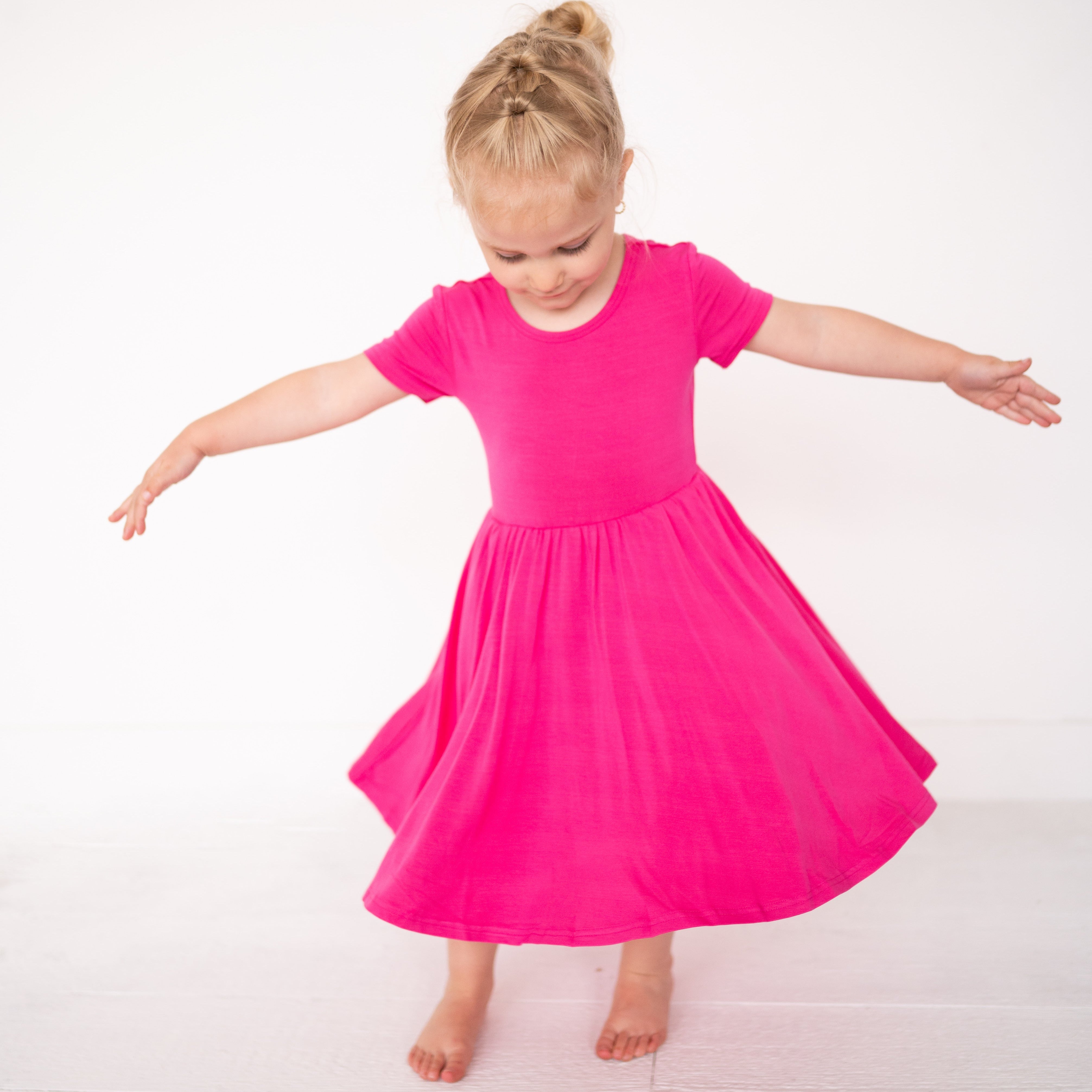 A young girl in a bright pink dress spins with her arms outstretched.