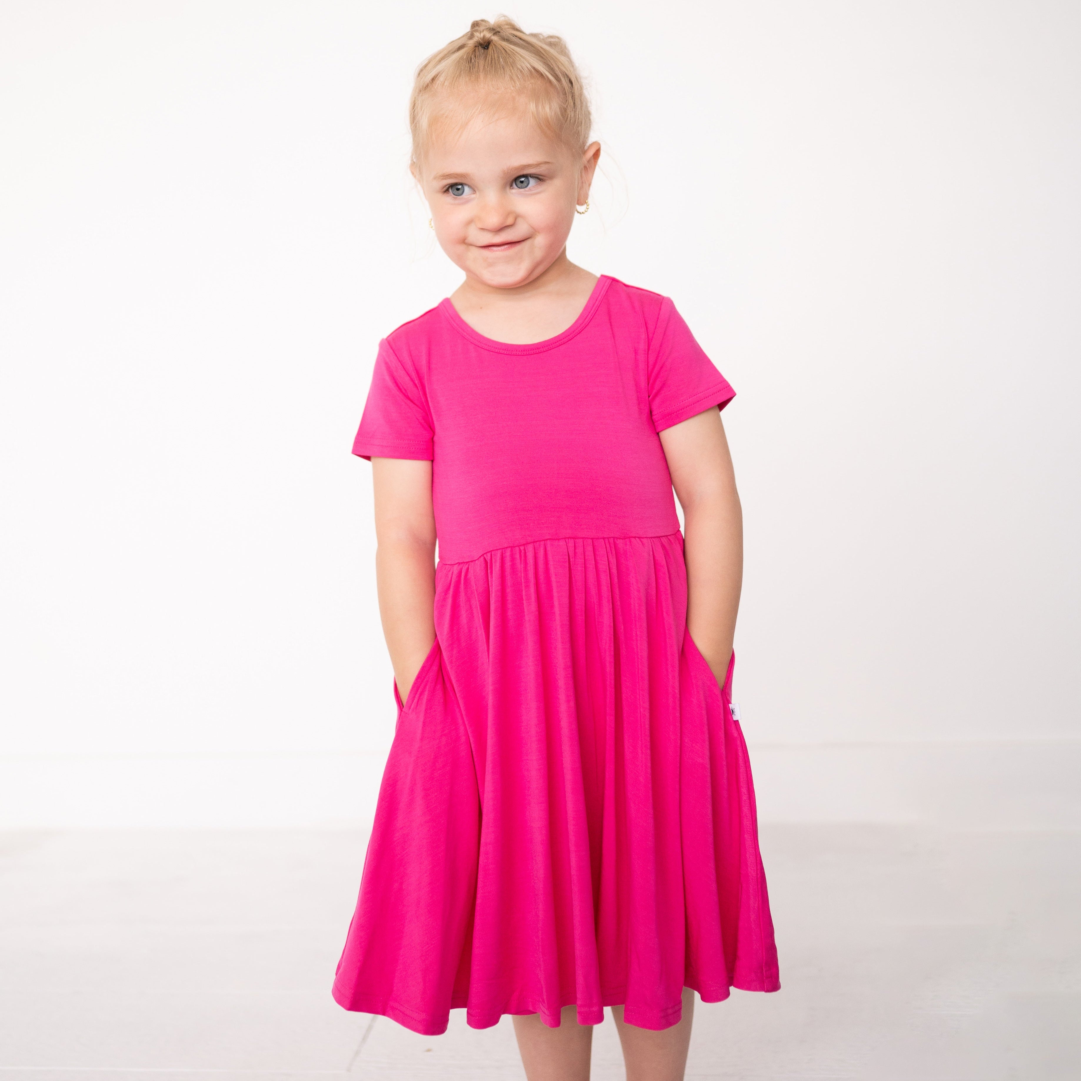 A young girl in a bright pink bamboo dress with pockets.