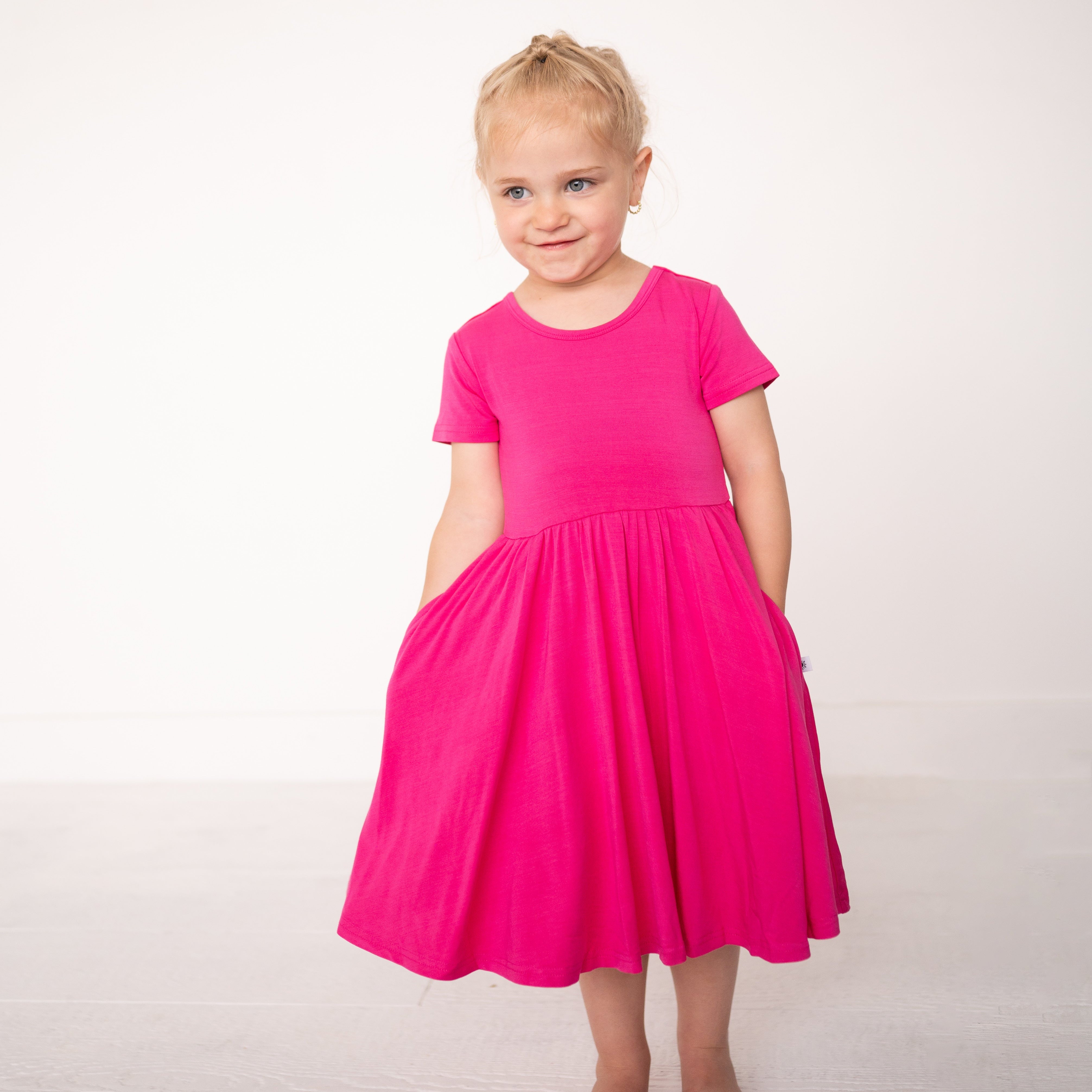 A young girl wears a bright pink bamboo dress with pockets.