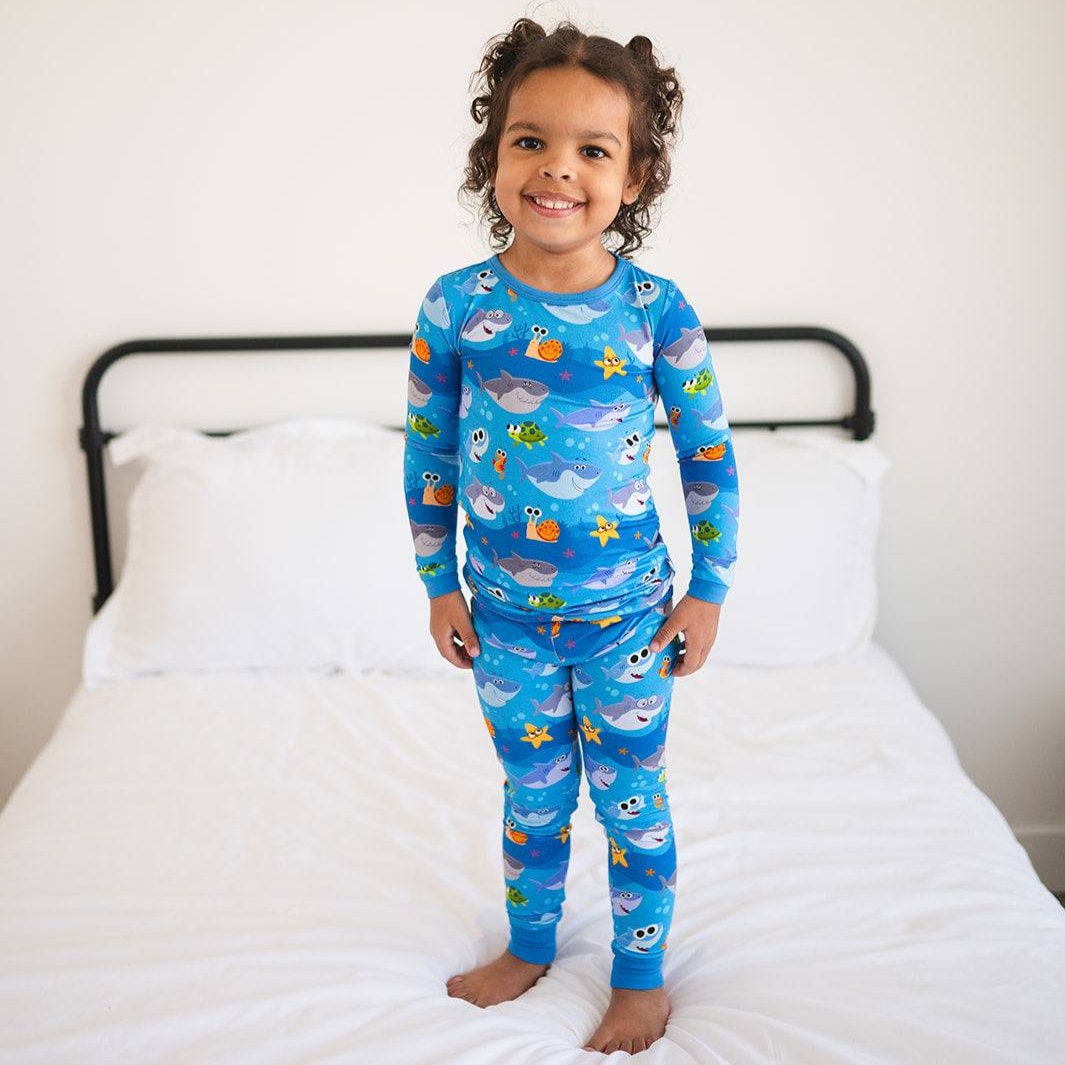 A young girl smiles in blue pajamas with a Baby Shark print.