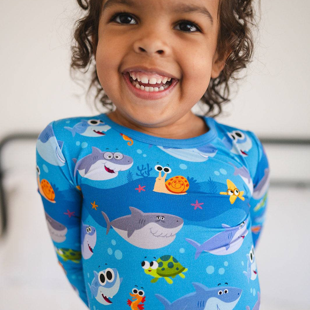 A young child smiles wearing blue pajamas with a Super Simple Baby Shark print.