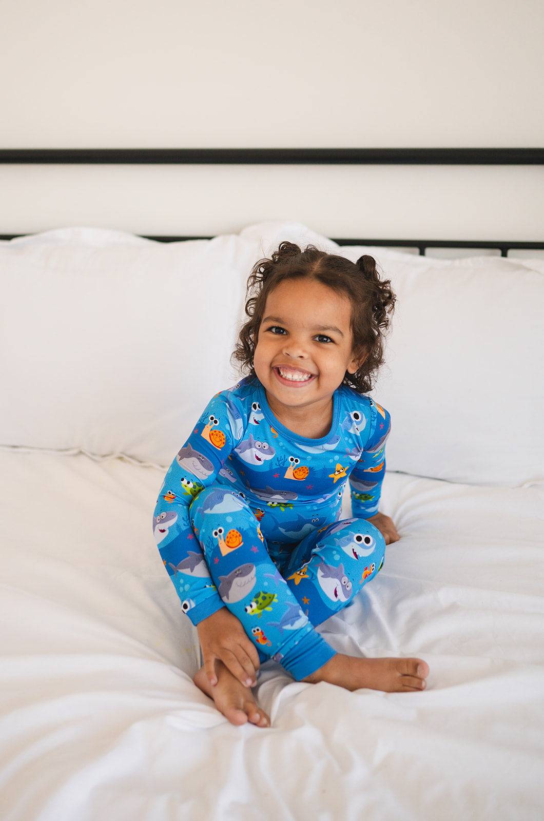 A young child smiles while wearing blue pajamas with a baby shark print.