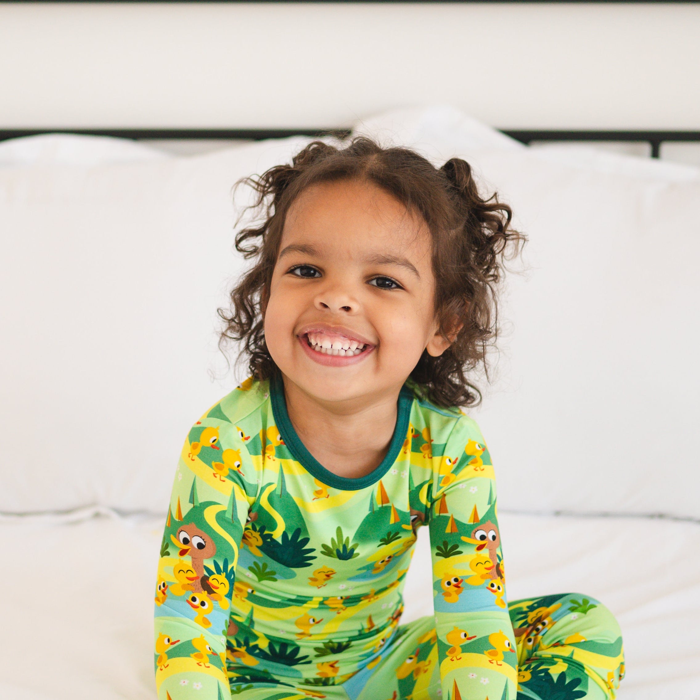 A young child smiles while wearing a green pajama set with a duckling print.