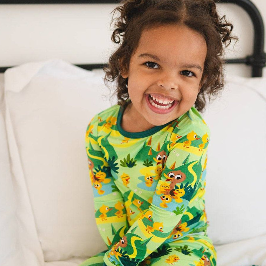 A young child smiles while wearing a green pajama set with a "5 Little Ducks" print.