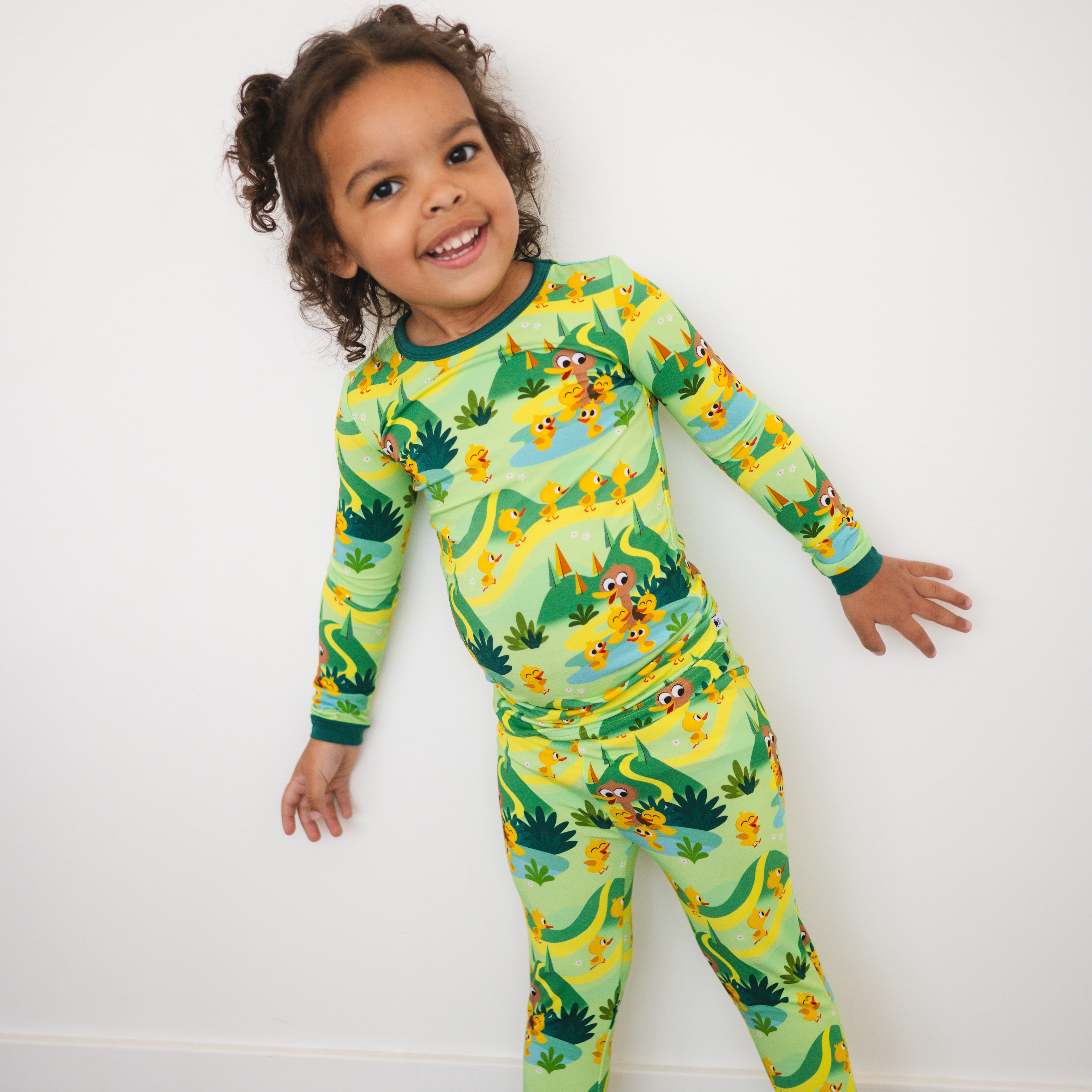 A young girl smiles in a green pajama set with a "5 Little Ducks" print.