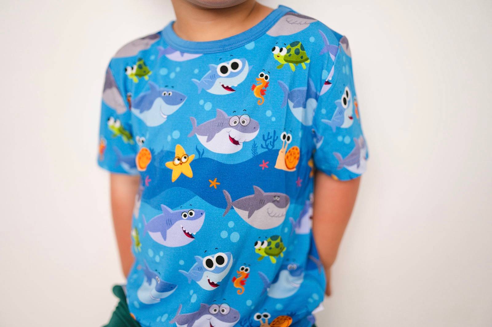 Blue t-shirt with a repeating pattern of cartoon sharks, turtles, starfish, and seahorses.