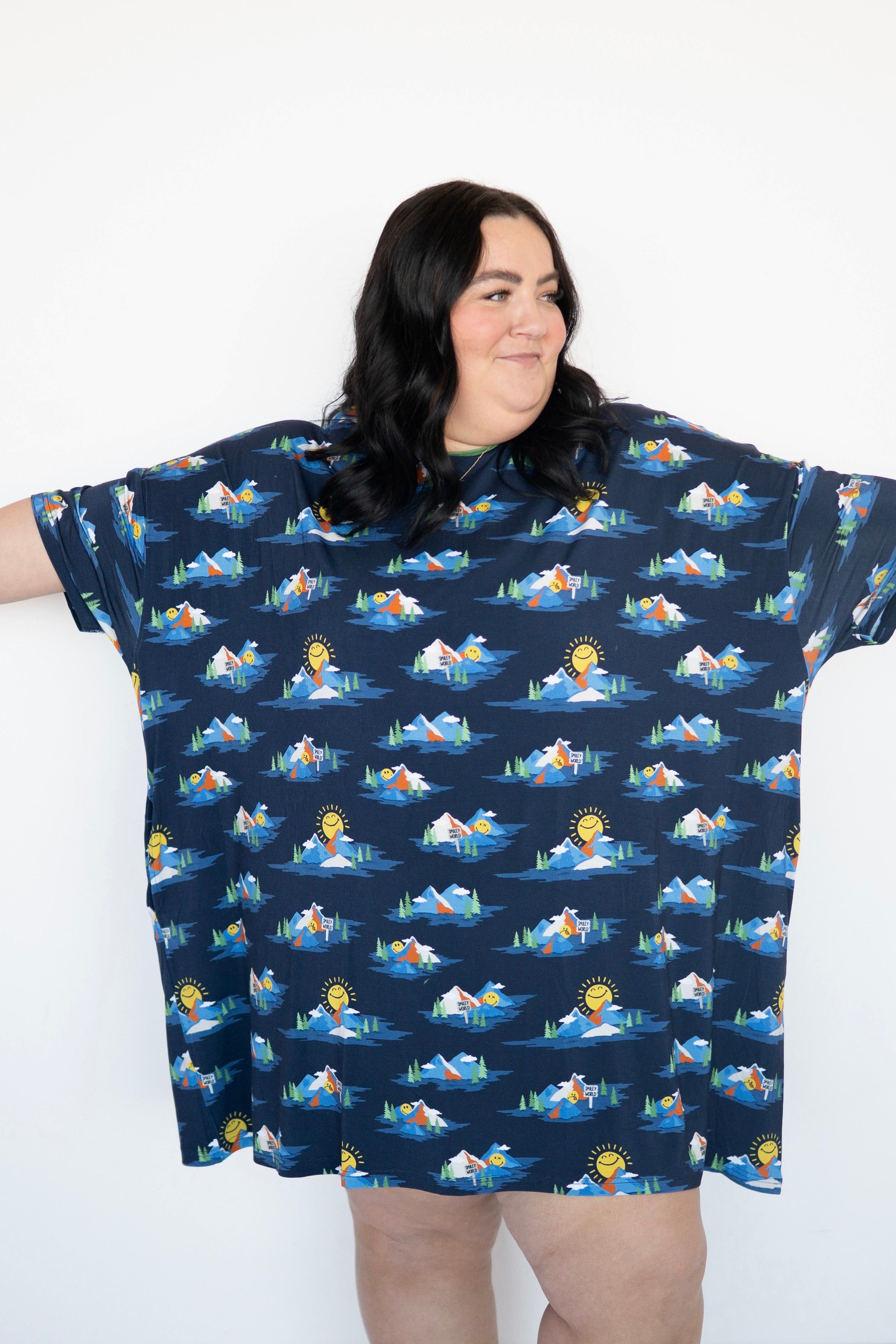A woman wears a navy blue oversized t-shirt with a repeating print of mountains, trees, and smiley faces.