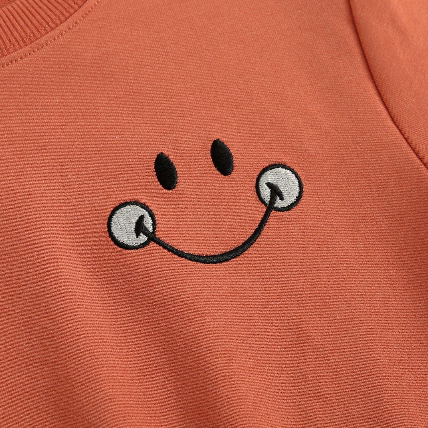Crewneck with embroidered Mini Smiley face in rust color.