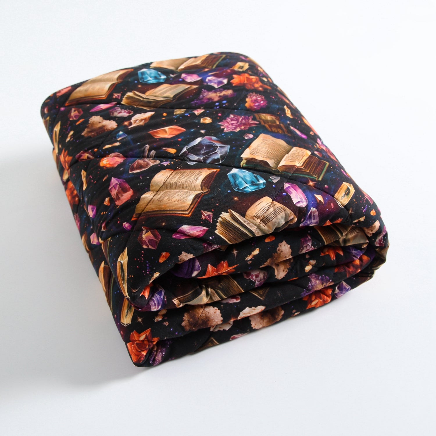 A folded quilt with a black background featuring an all-over print of open books and colorful crystals.