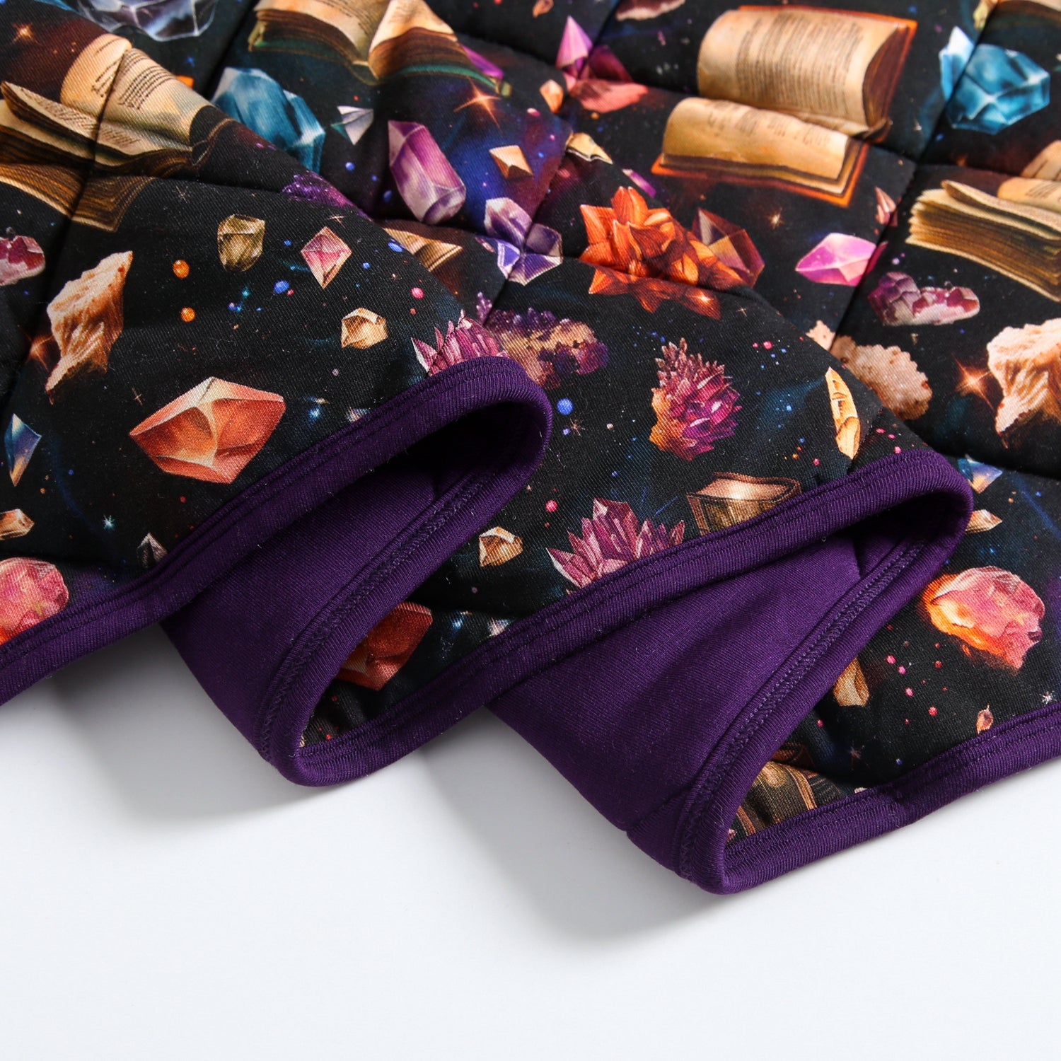 A quilted blanket with a cosmic crystal and book print and purple trim.