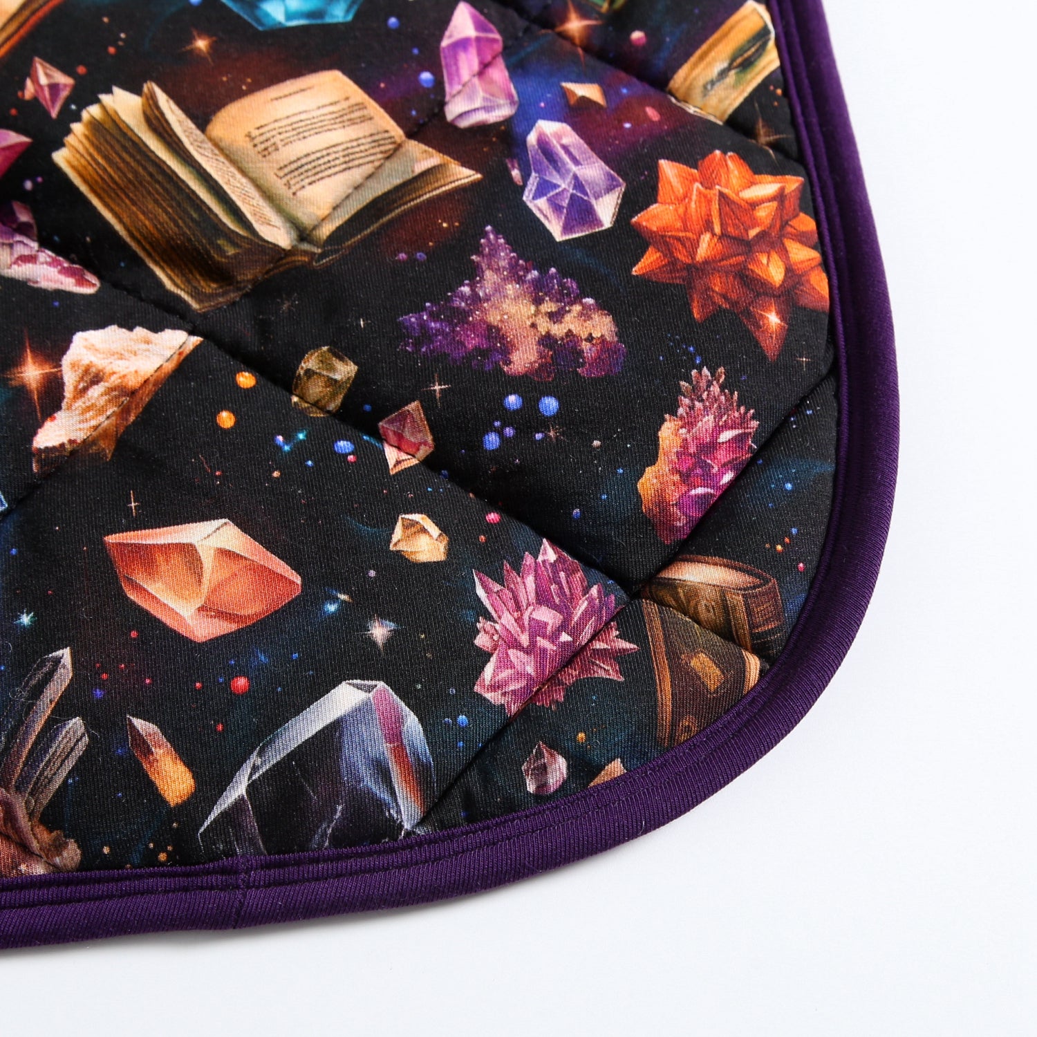 A quilted blanket with a cosmic print of crystals and books, edged in purple.