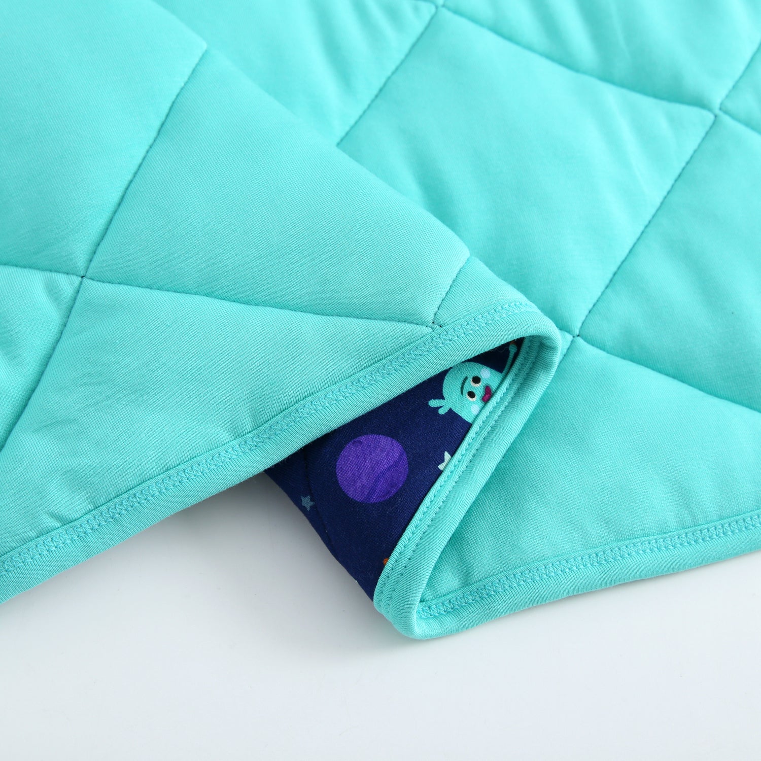 A quilted turquoise blanket with a space-themed print peeking out.