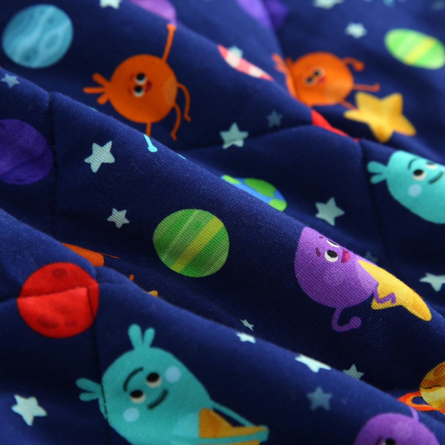 A quilted blanket with a dark blue space-themed print featuring cartoon aliens and planets.