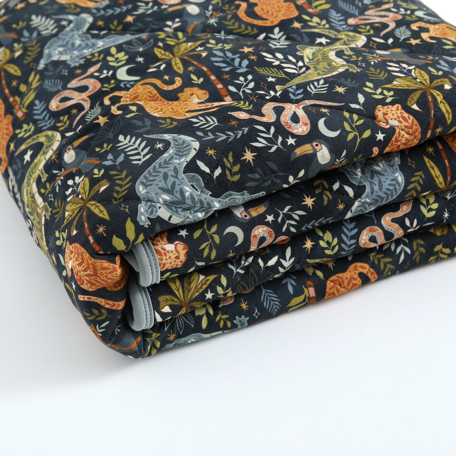 A folded quilt with a dark background and a jungle-themed print featuring animals and plants.