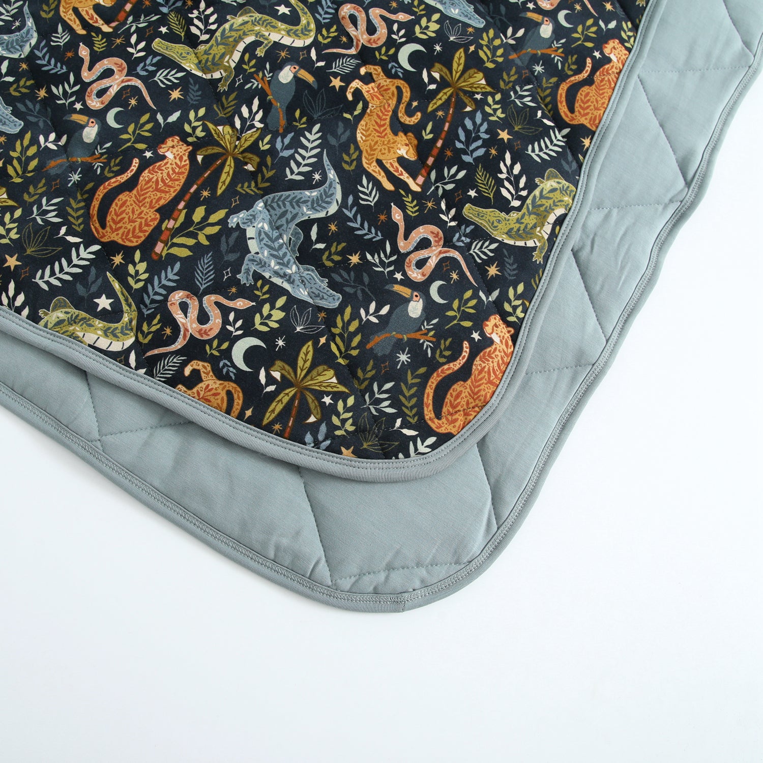 A quilted blanket with a dark jungle print featuring leopards, snakes, and toucans, bordered by light blue fabric.