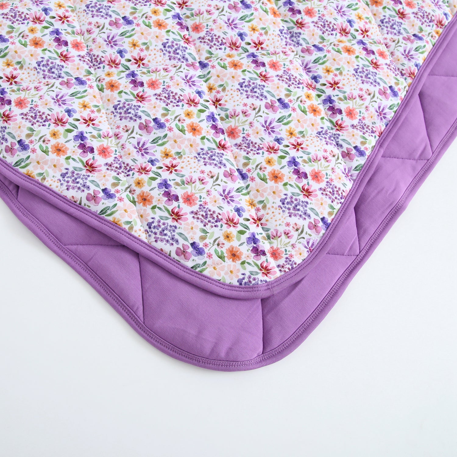 A quilted blanket with a dainty floral pattern and a purple border.