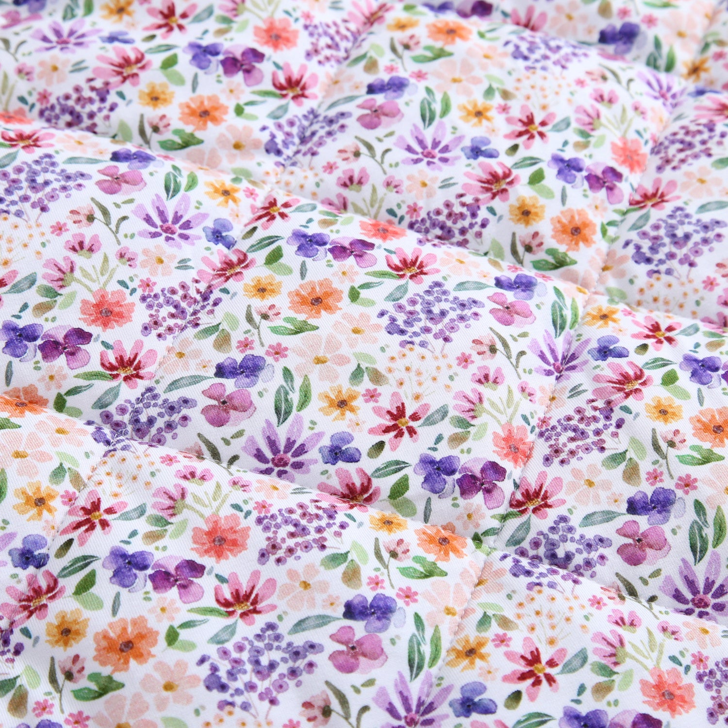 A quilted couch throw with a dainty floral pattern in pink, purple, and orange.