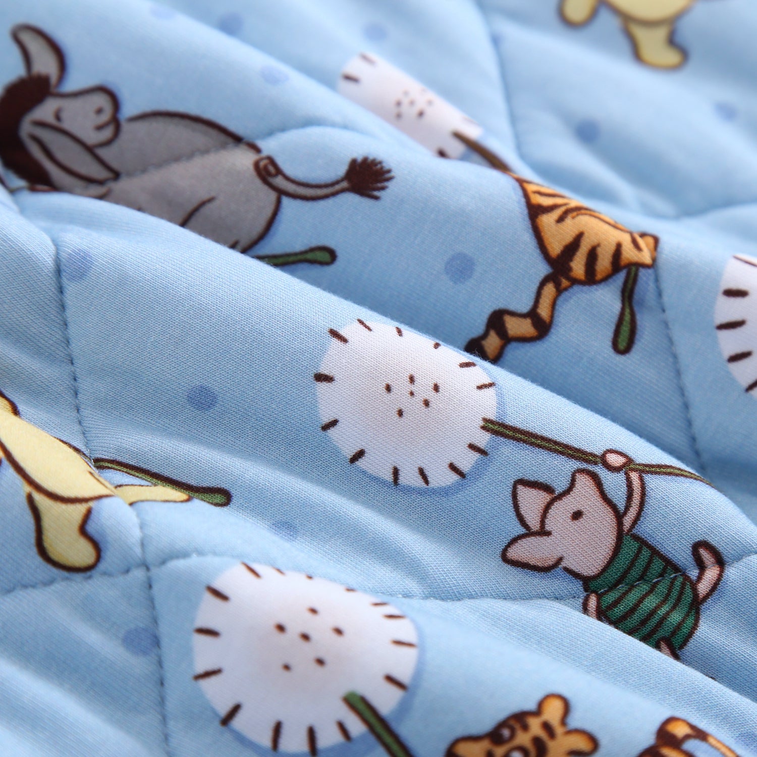 A light blue quilted blanket with a pattern of Winnie the Pooh characters.