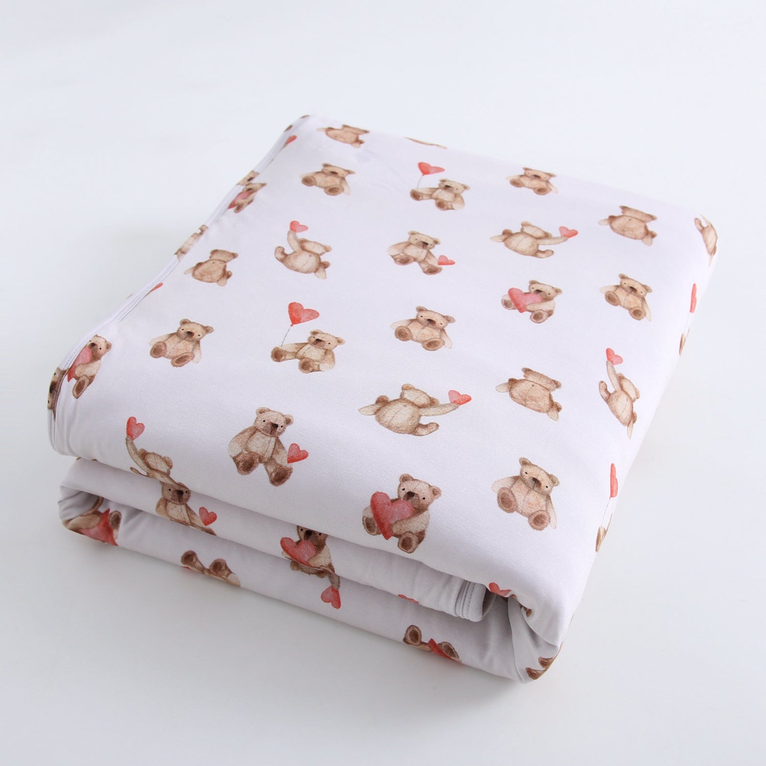 A folded white blanket with a pattern of watercolor teddy bears holding hearts.