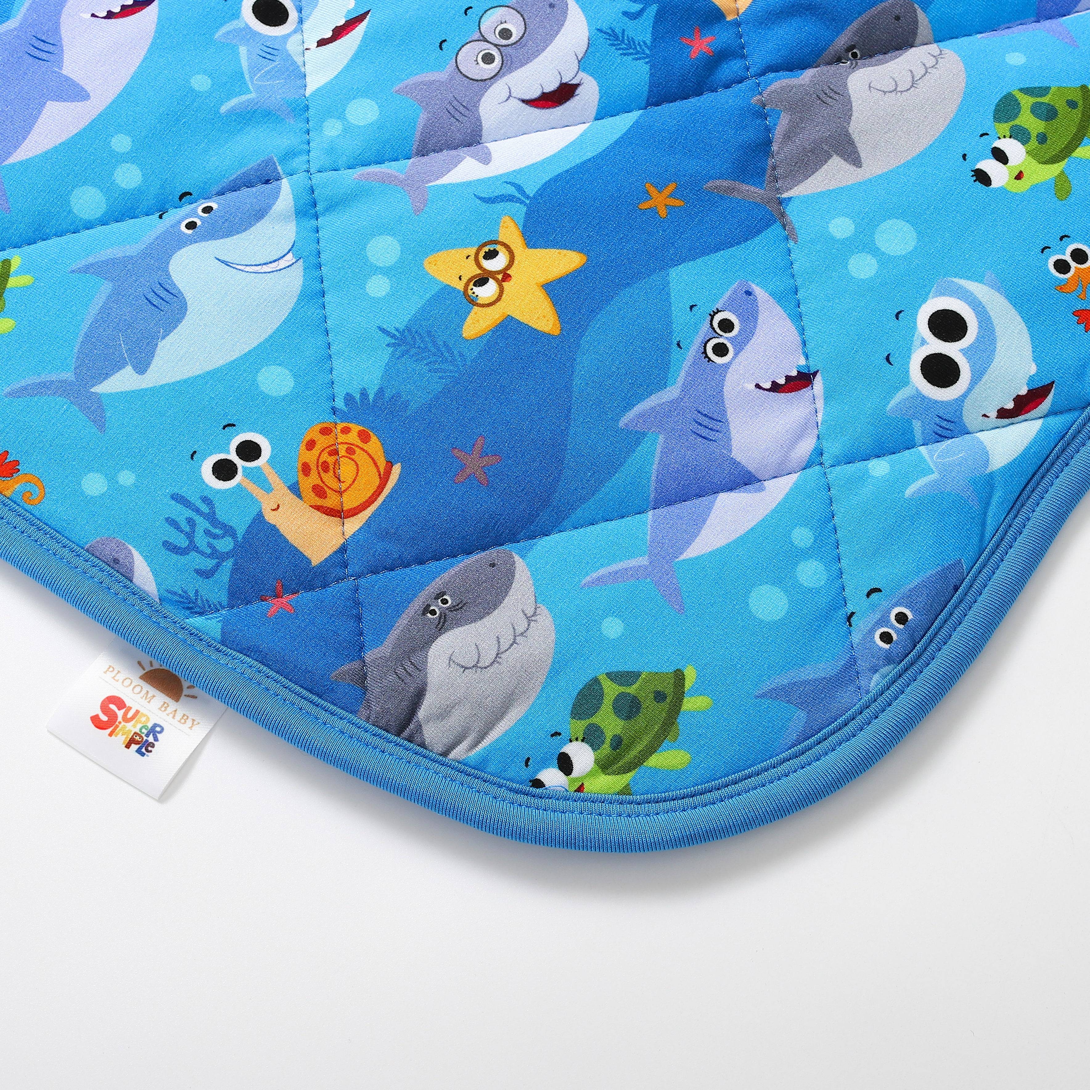 A quilted baby blanket with a blue background featuring cartoon sharks, a turtle, a starfish, and a snail.